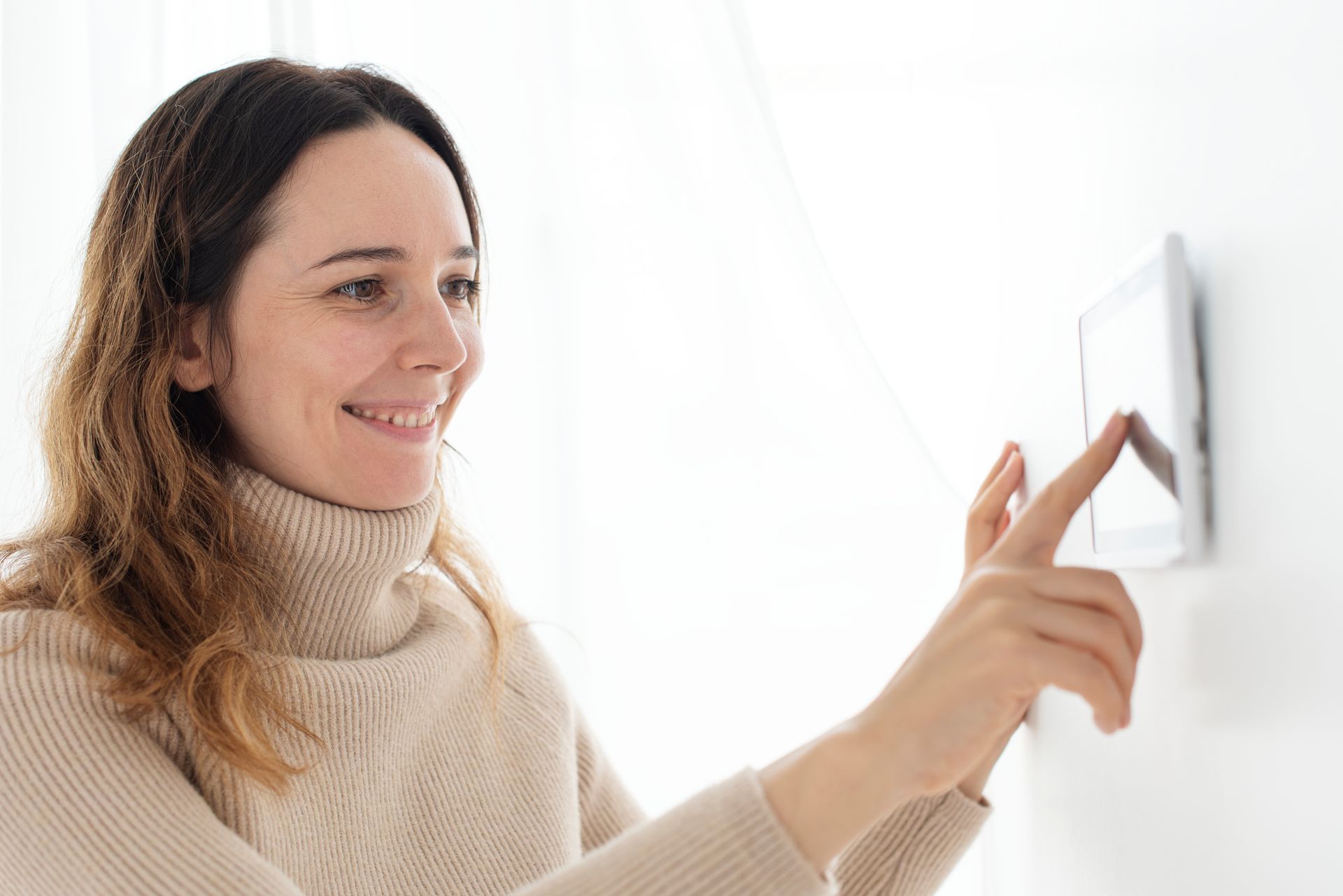 Woman in a beige sweater smiling while pressing a light switch on a white wall