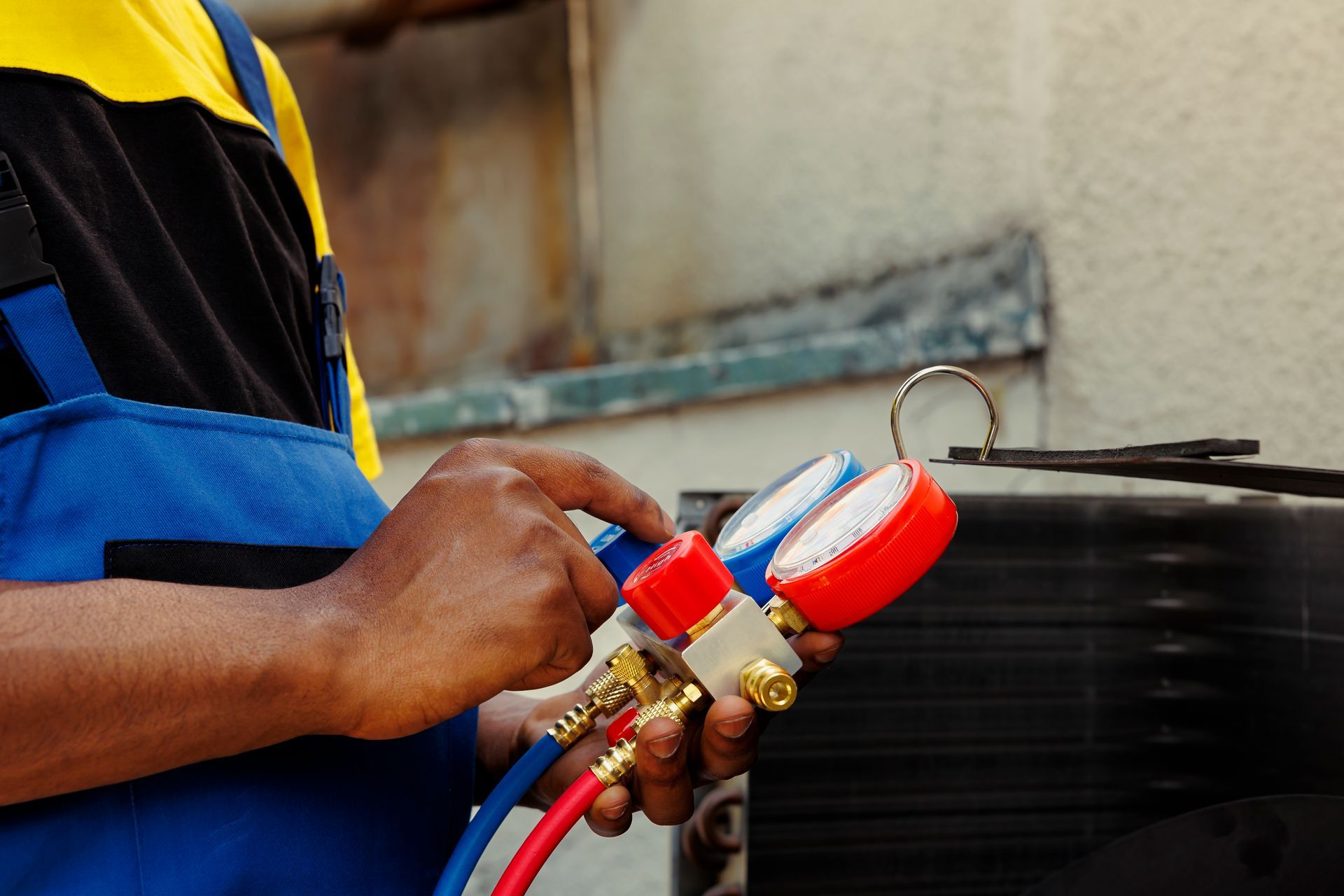 Technician adjusting gauges on red and blue hoses connected to outdoor equipment