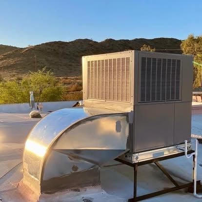 Rooftop HVAC unit with metal ductwork, against a backdrop of desert mountains under a clear sky.