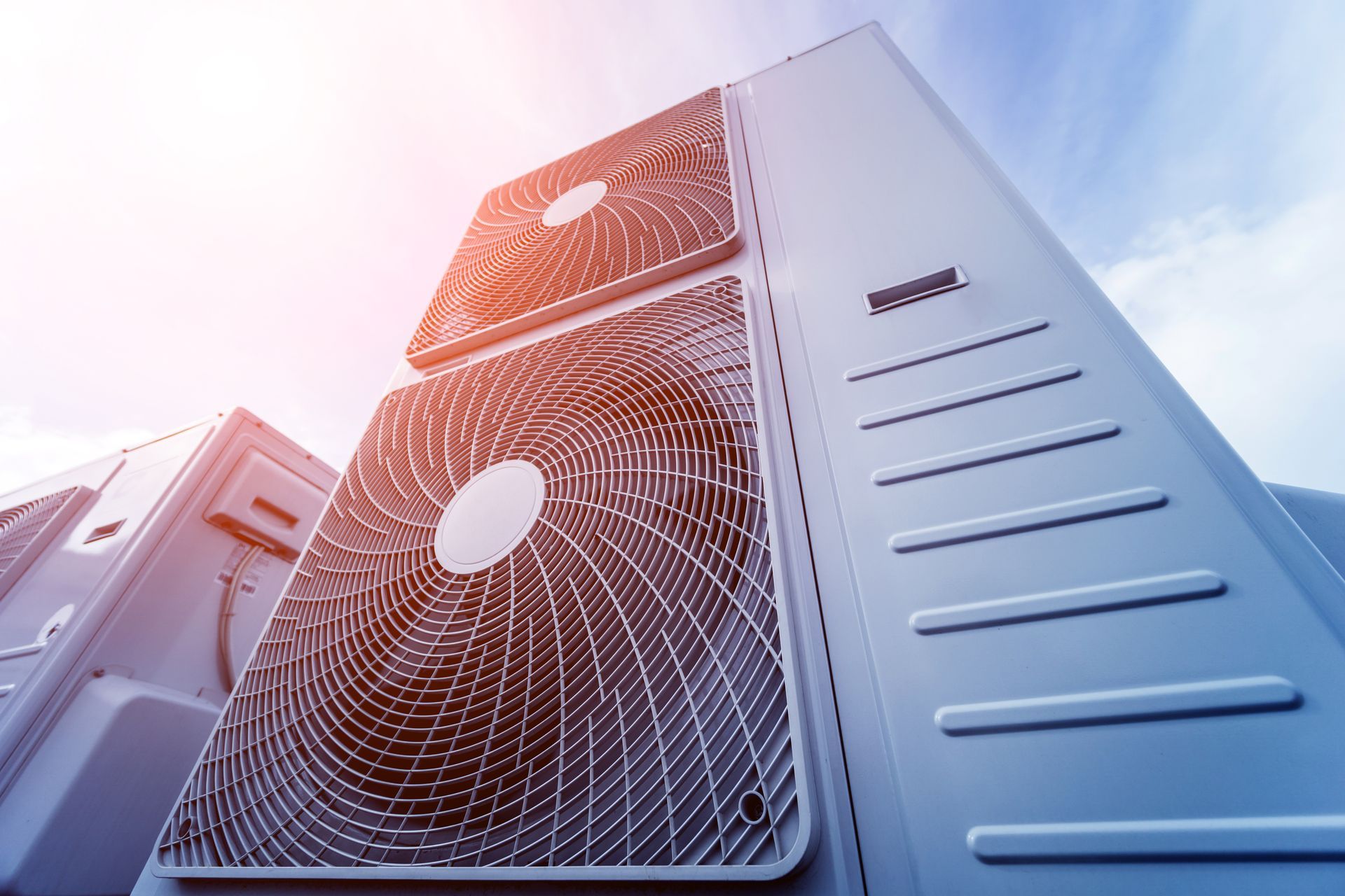 Stacked outdoor HVAC units with metal grilles against a bright blue sky