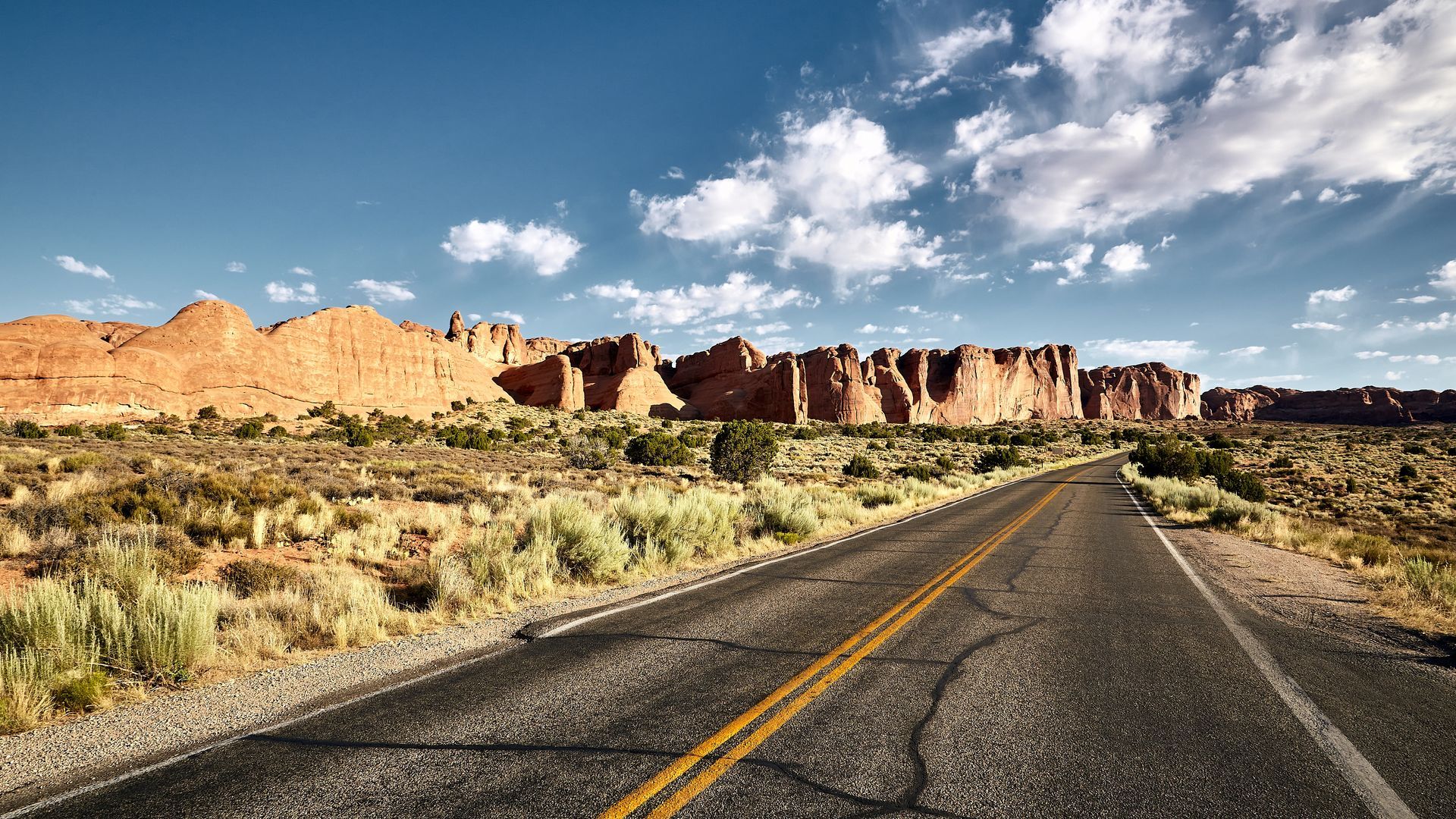 an empty road in the desert with mountains in the background .