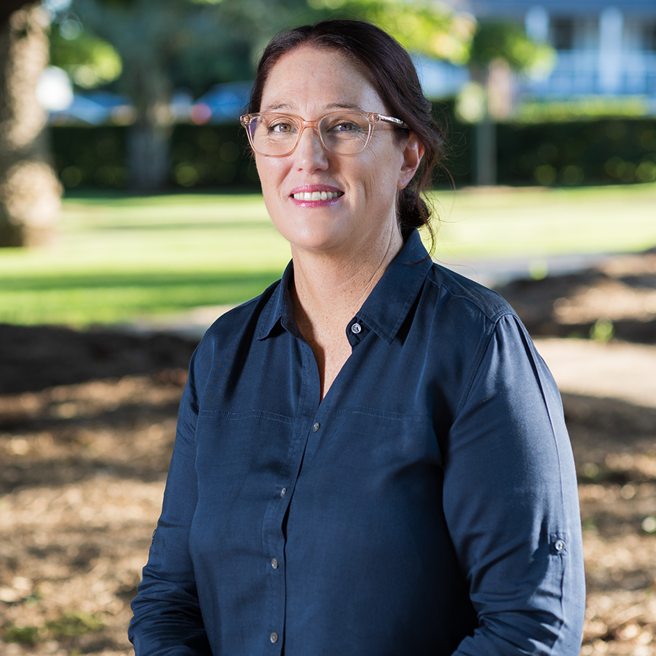 A headshot photograph of the Trilogy Home Care Director, Kellie Curtis. She is smiling, wearing glasses and a navy blouse.