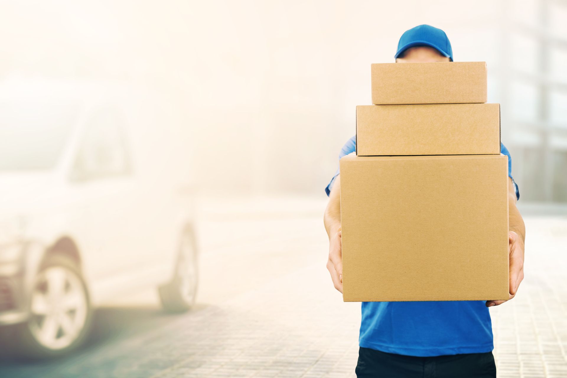 Delivery person holding a stack of three cardboard boxes near a vehicle.