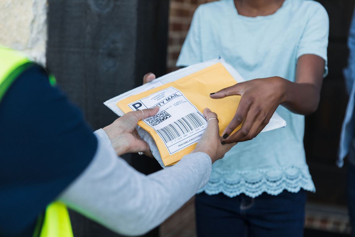 Delivery person in blue uniform hands package to woman at doorway.
