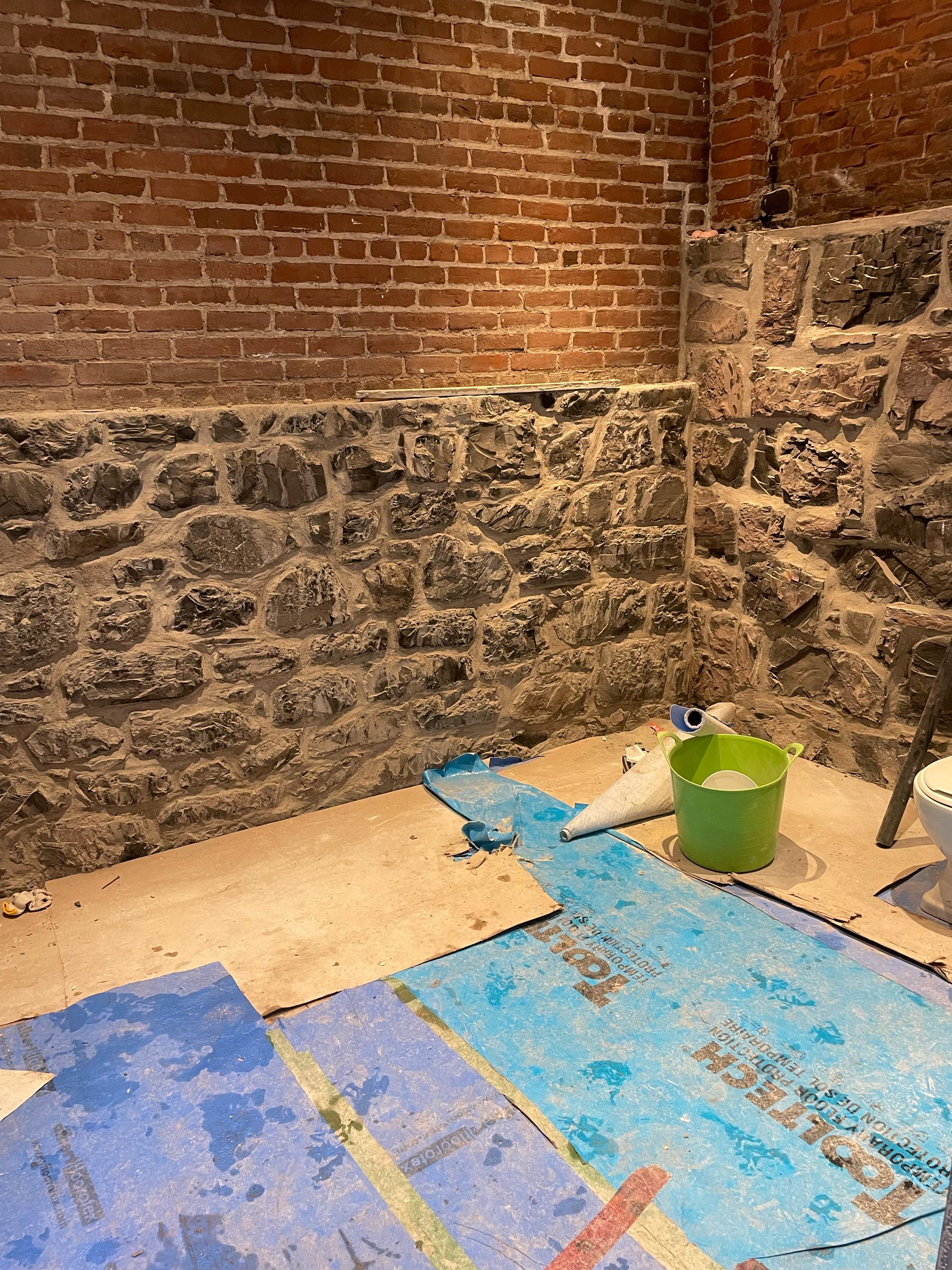 Une salle de bain avec un mur de briques et une bâche bleue au sol.