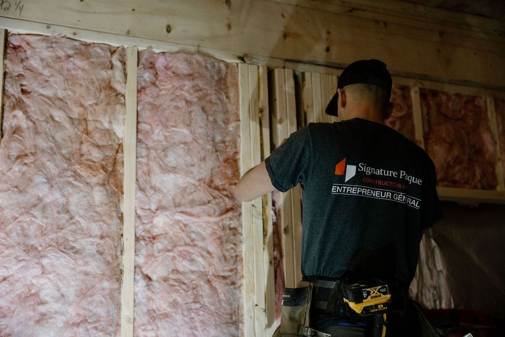 Un homme installe une isolation rose entre des montants en bois dans une pièce en construction.