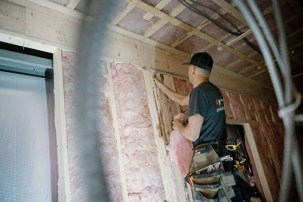 Ouvrier du bâtiment installant une isolation rose dans un mur, décor intérieur.
