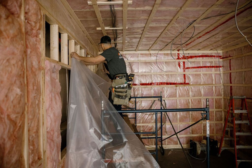 Ouvrier du bâtiment installant une bâche en plastique sur l'isolation dans une pièce en construction.