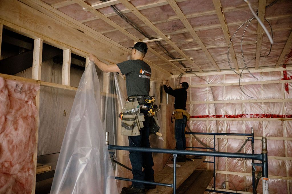 Deux ouvriers du bâtiment installent des bâches en plastique sur un mur et un plafond à l'intérieur d'un bâtiment.