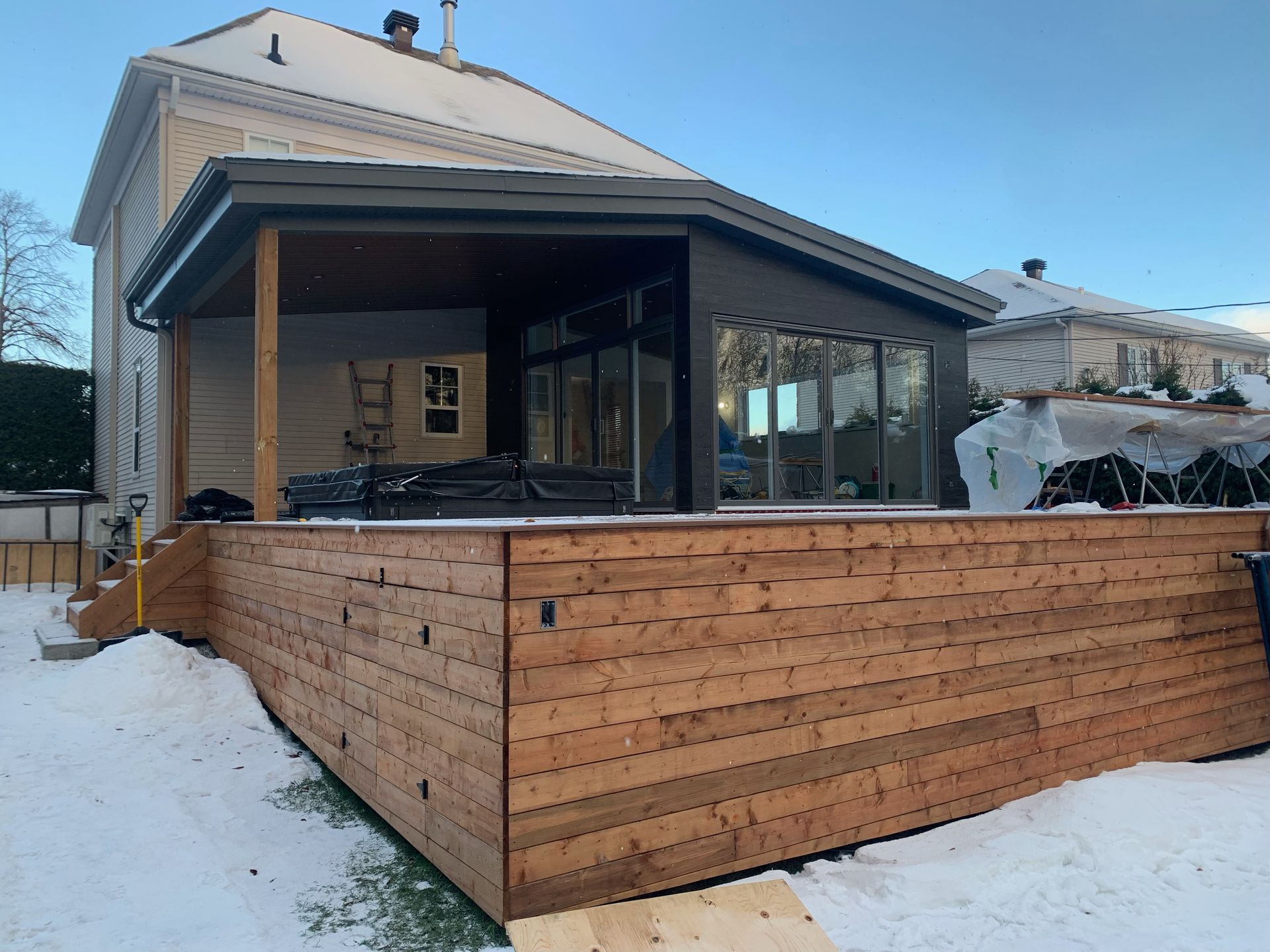 Une maison avec une terrasse en bois devant dans la neige.