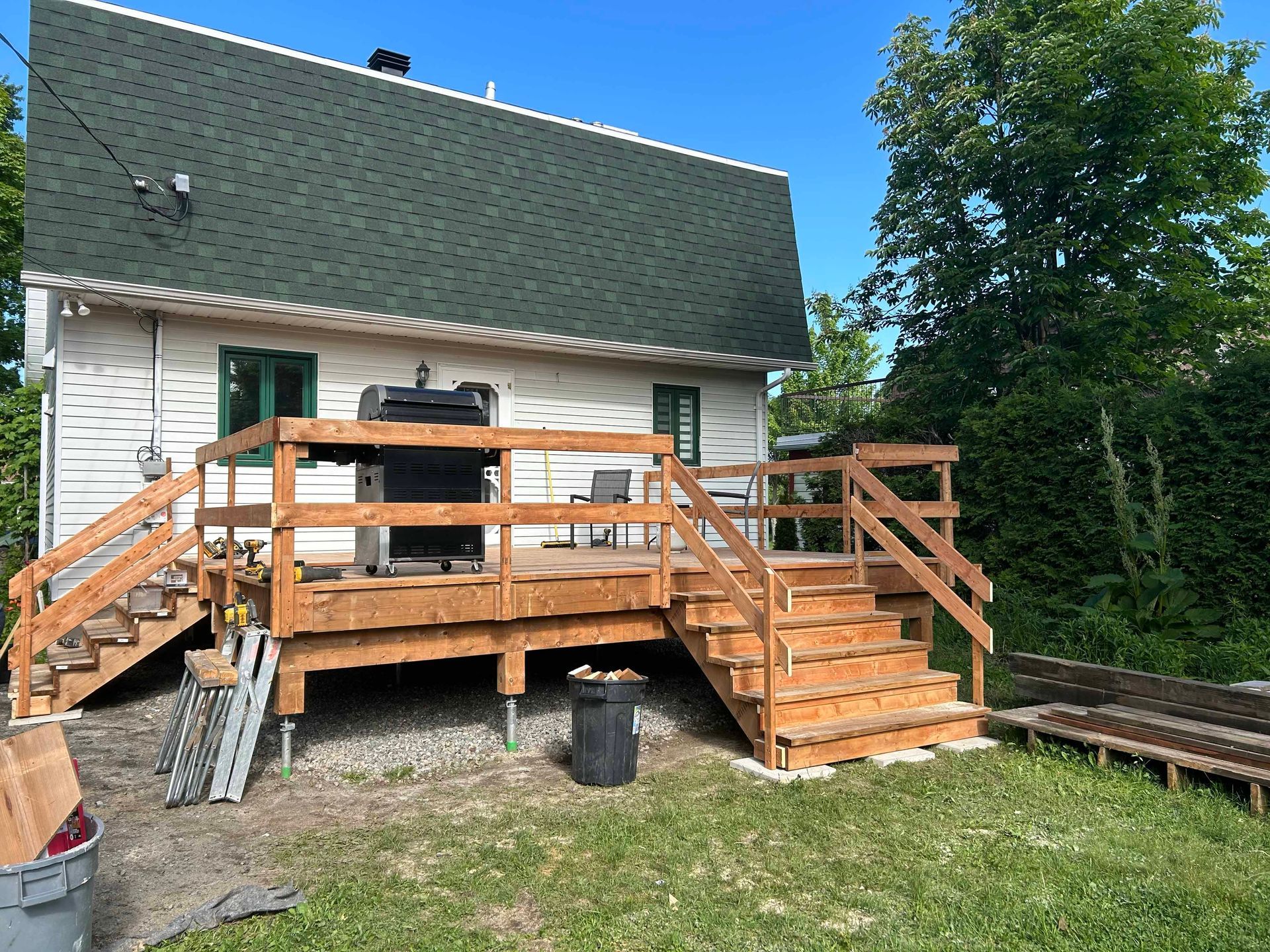 Terrasse en bois avec escalier attenante à une maison blanche au toit végétalisé, sur un espace gazonné.
