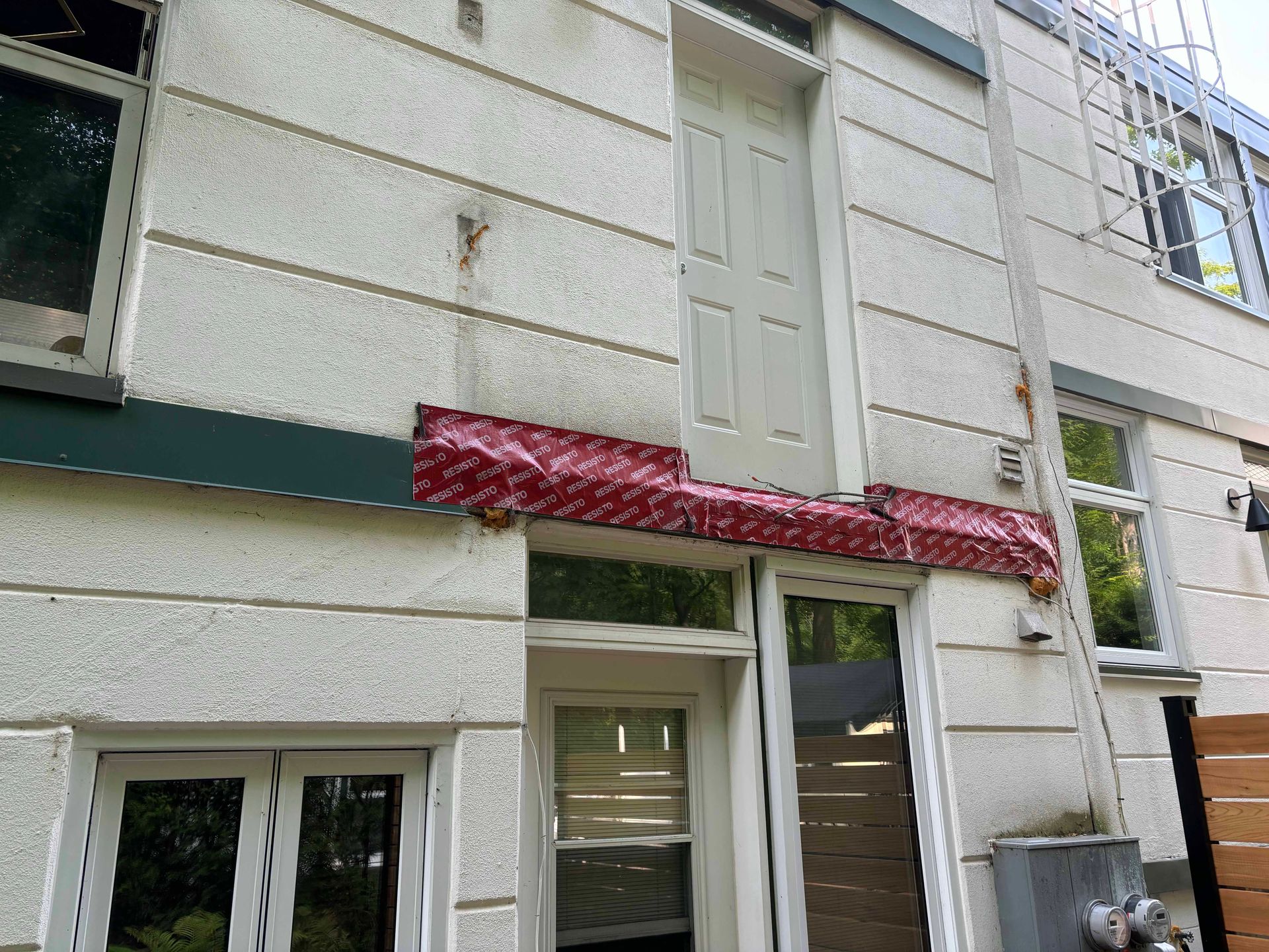 Extérieur du bâtiment avec façade en stuc blanc et solins rouges. Une porte se trouve au-dessus d'une autre.