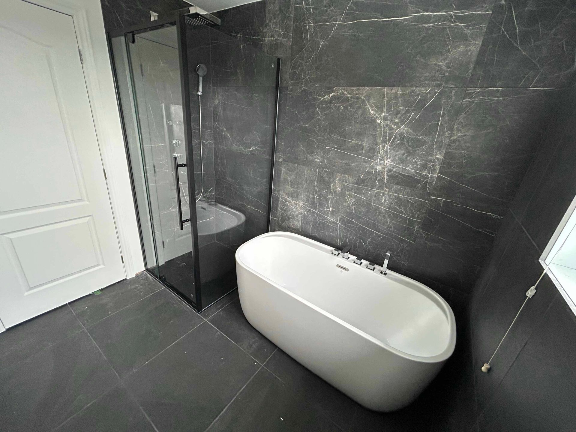 Une salle de bain moderne avec une baignoire blanche, une douche noire, des murs gris foncé et une porte blanche.