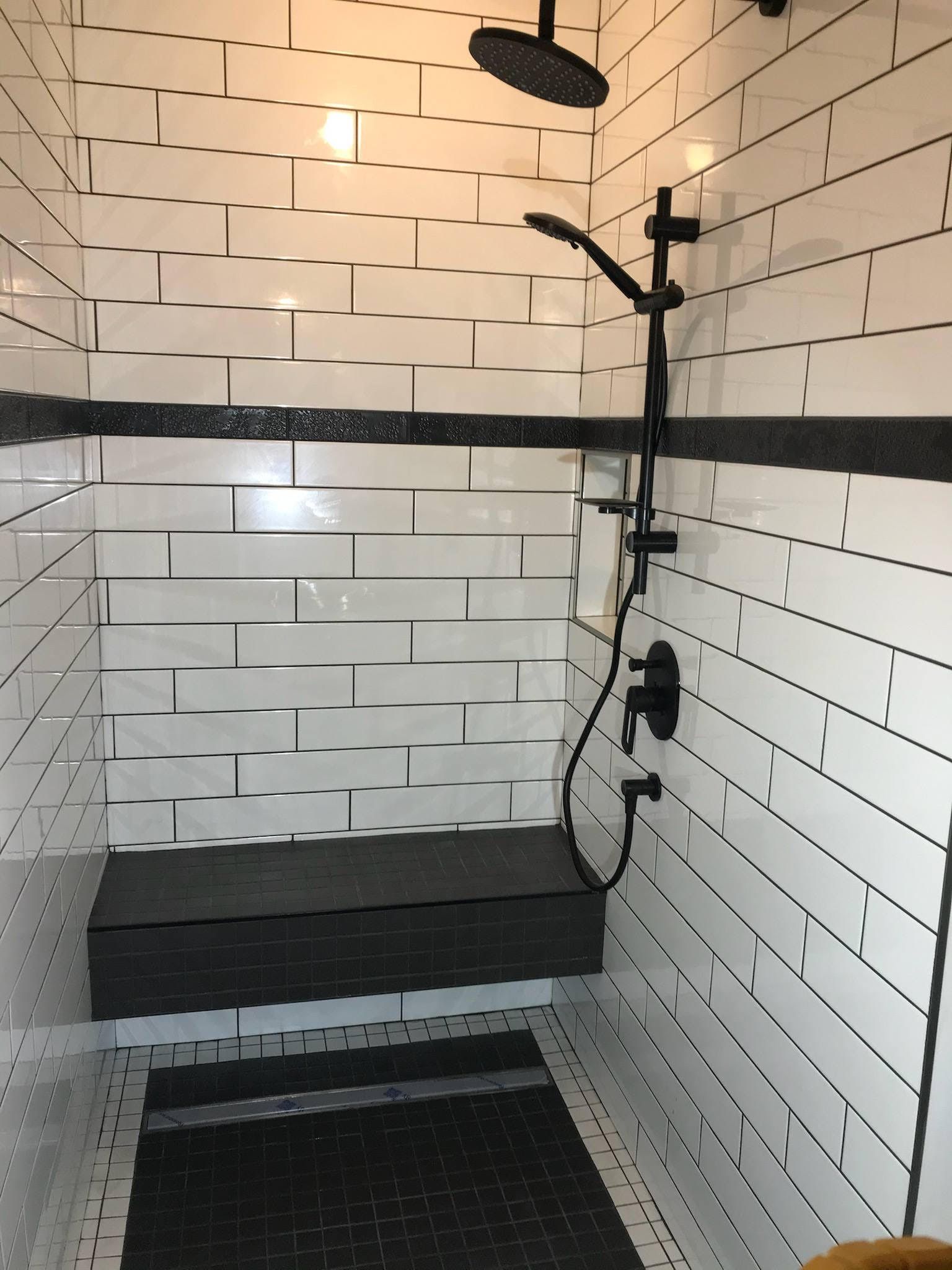 Une douche avec du carrelage blanc et une pomme de douche noire