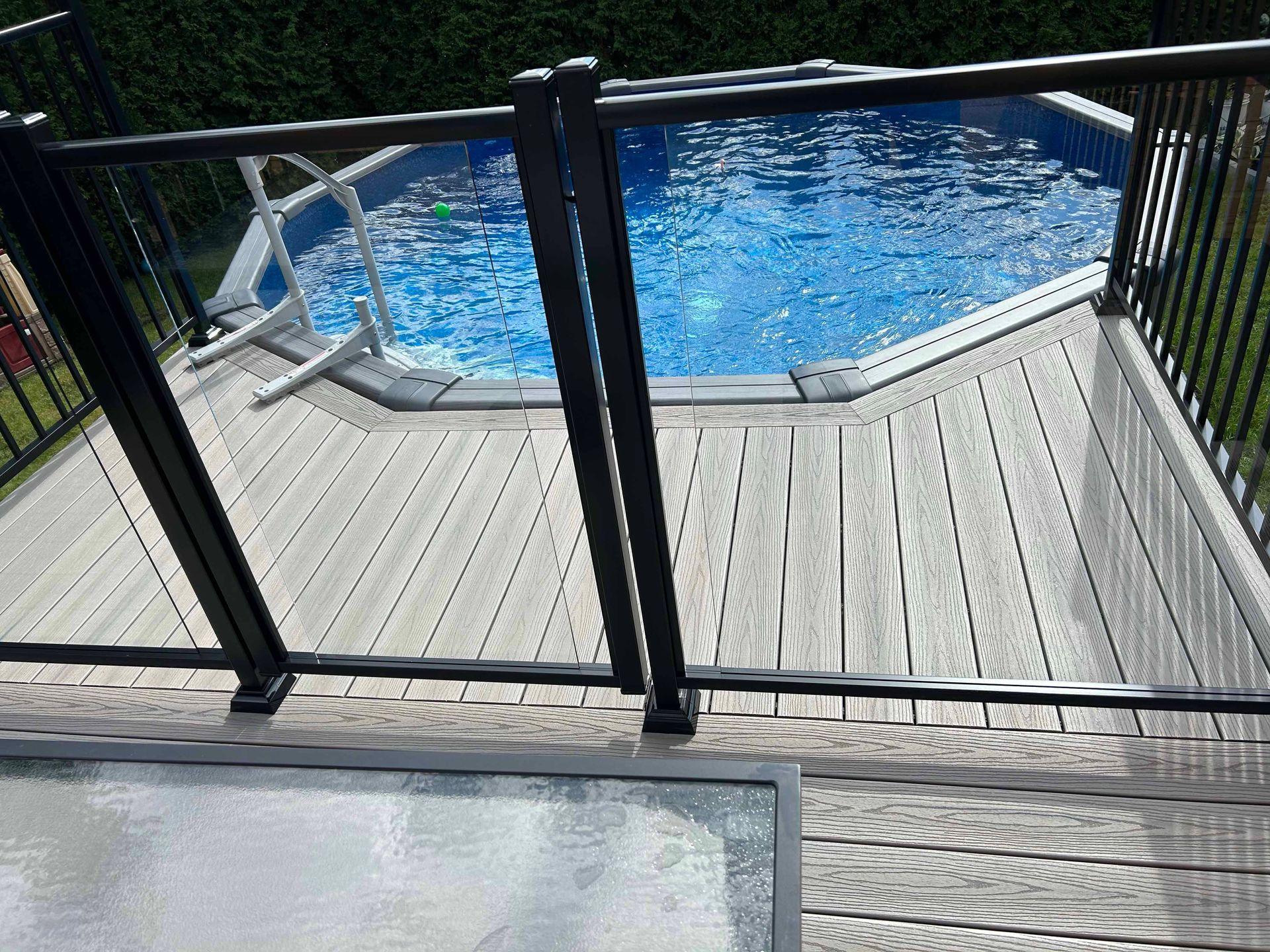 Piscine hors terre avec terrasse grise et garde-corps noir, eau bleue.