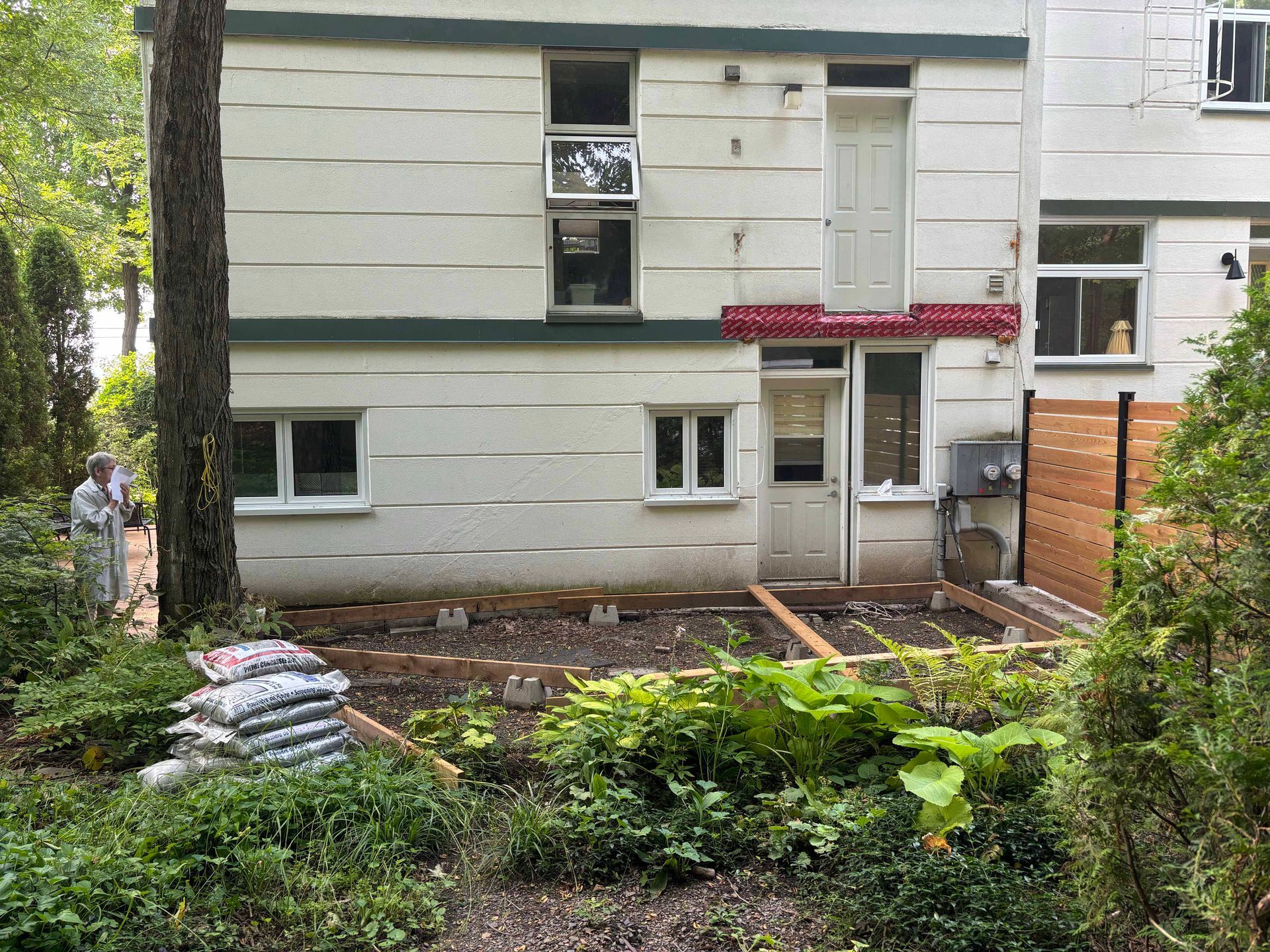 Arrière d'un immeuble de deux étages avec une terrasse en construction. Sacs de terre au premier plan, personne à l'arrière-plan.