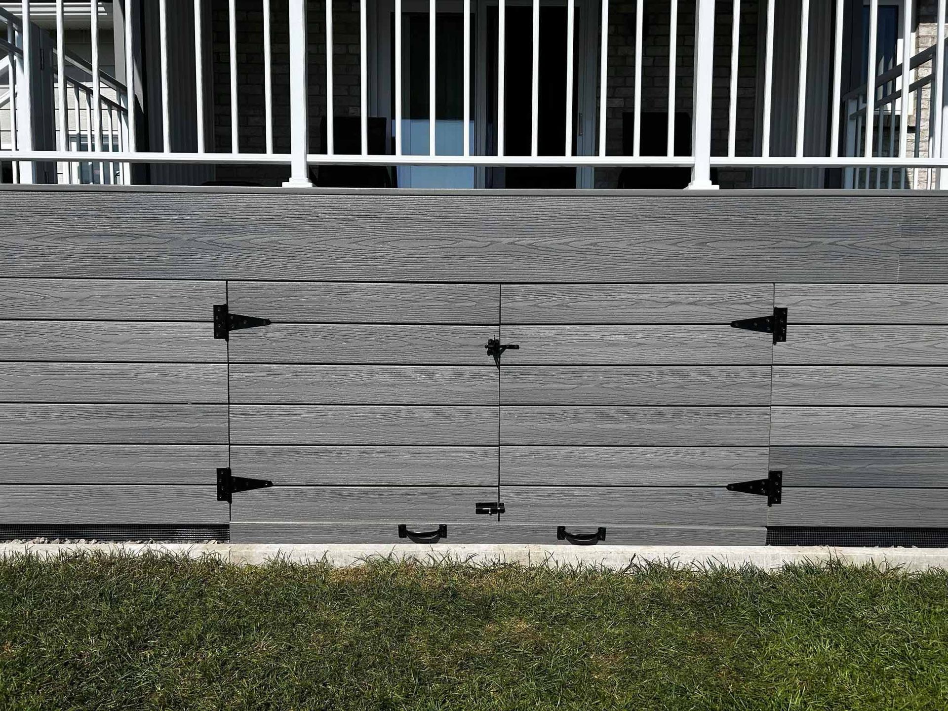 Façade de terrasse grise avec portes de rangement; balustrade blanche au-dessus, herbe verte en dessous.