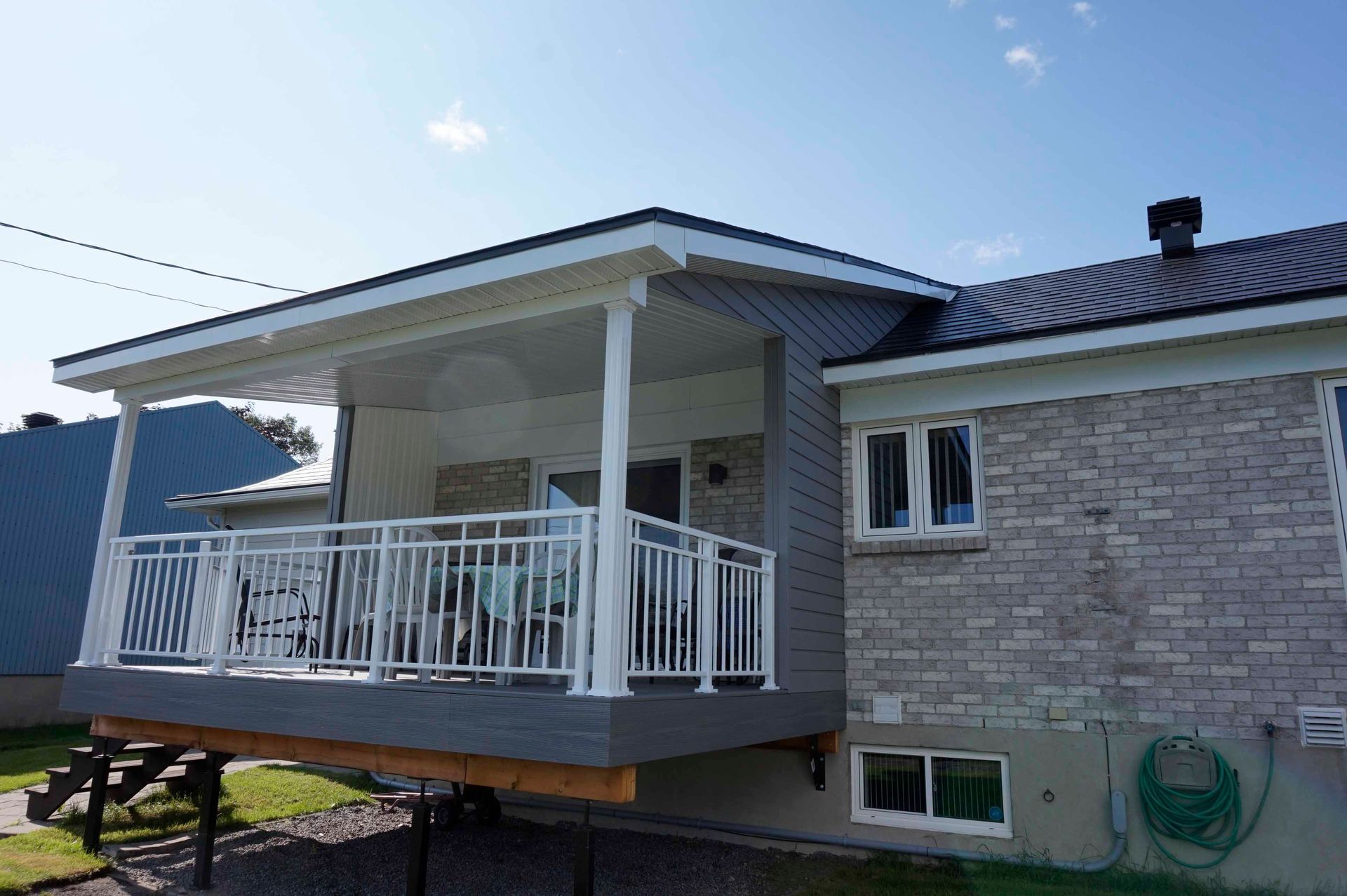 Une maison avec une terrasse grise et une balustrade blanche. La maison est en briques et dispose d'un patio couvert.