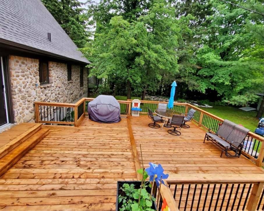 Une grande terrasse en bois avec un canapé, des chaises, un parasol et un grill.