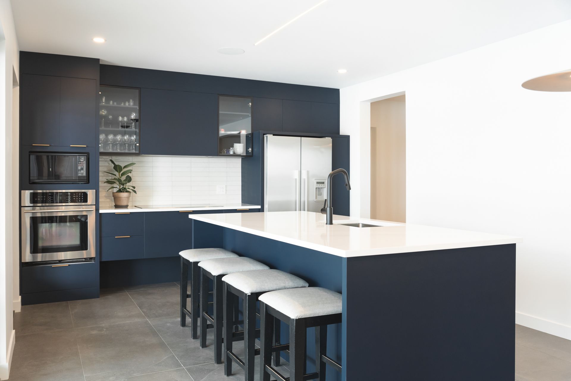 Cuisine moderne avec armoires bleu marine, îlot de comptoir blanc avec tabourets, appareils électroménagers en acier inoxydable et sol en béton.