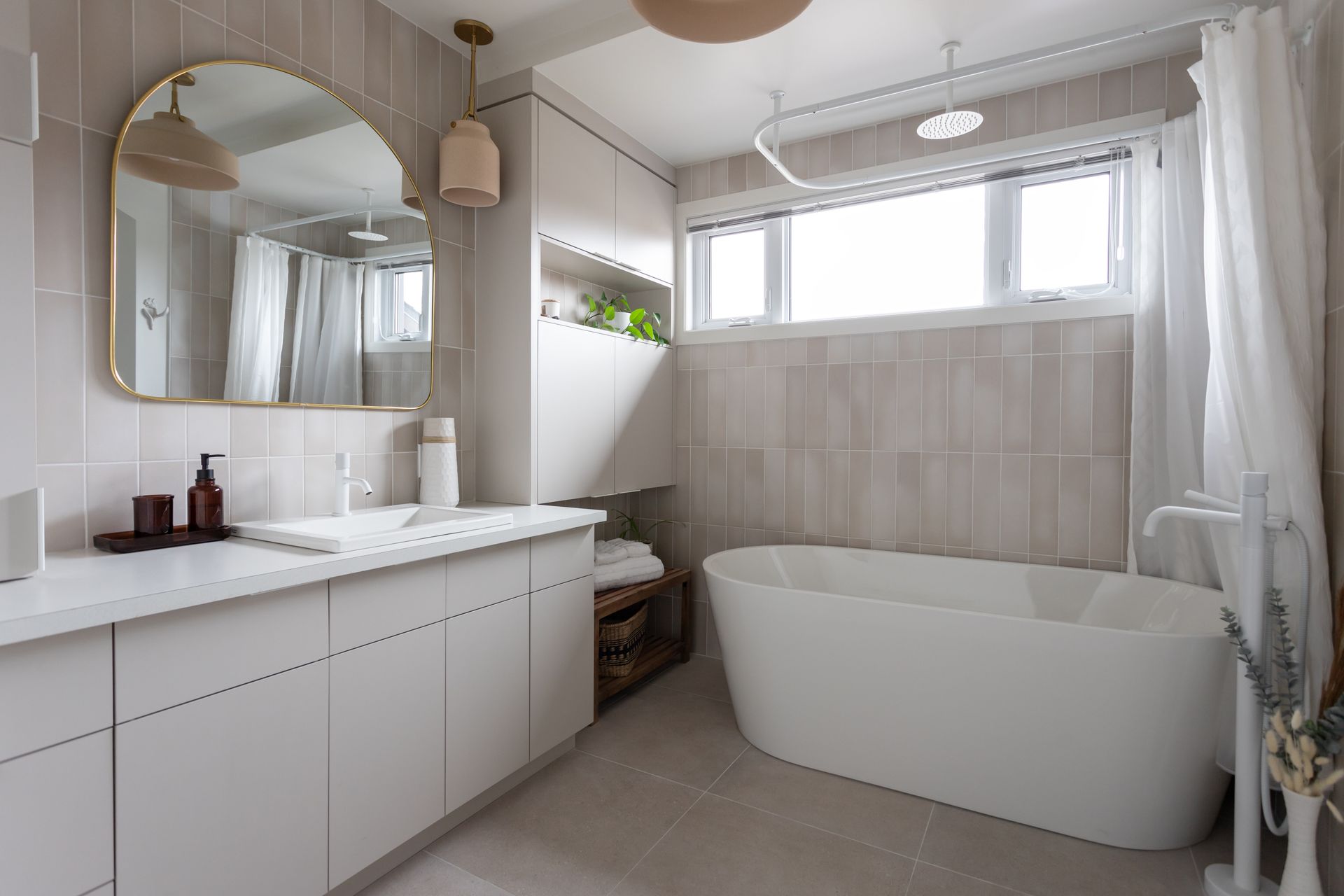 Salle de bain moderne aux tons neutres avec baignoire autoportante, grande fenêtre et vanité blanche.