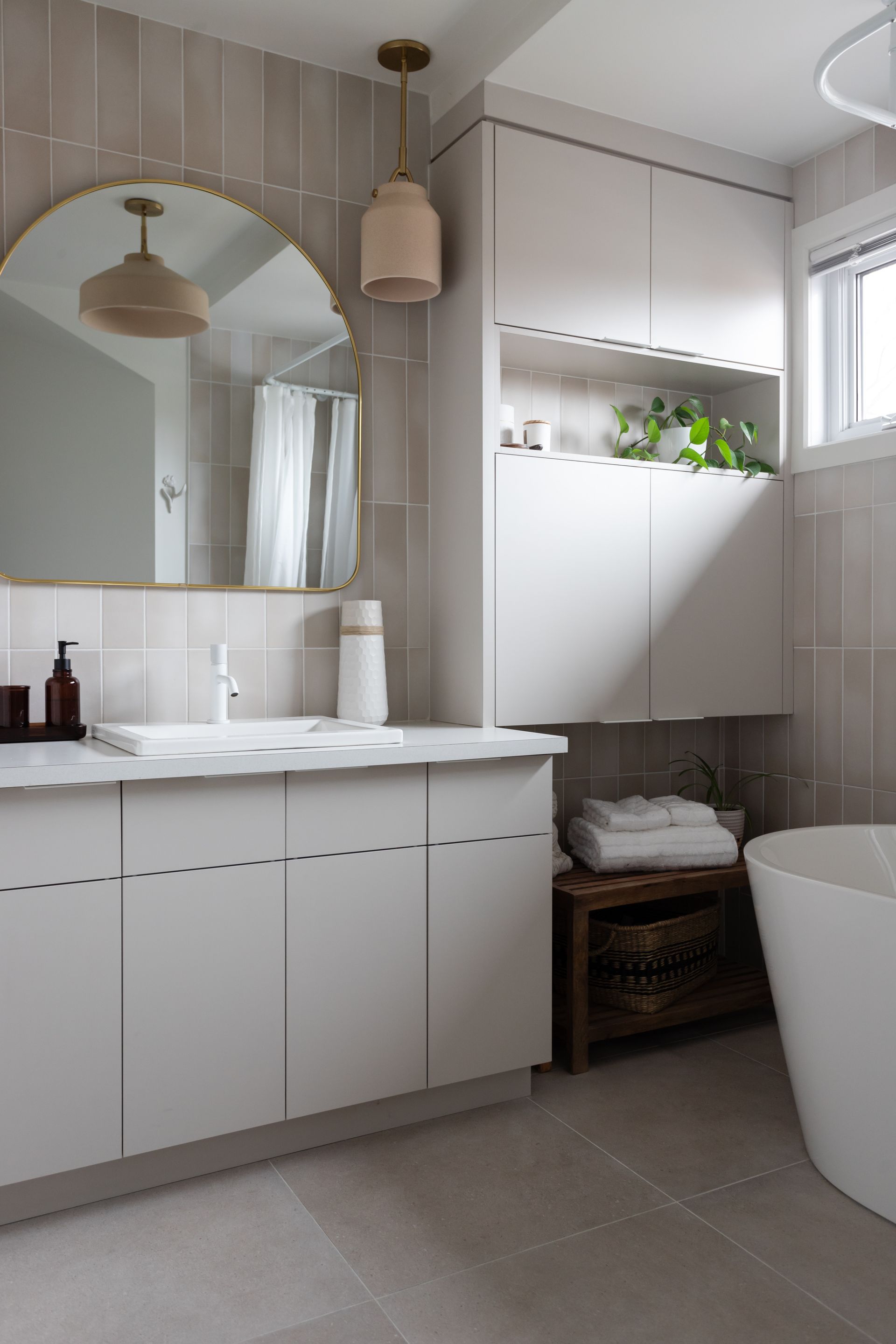 Salle de bain moderne avec armoires blanches, comptoir en marbre, miroir rond et baignoire autoportante.