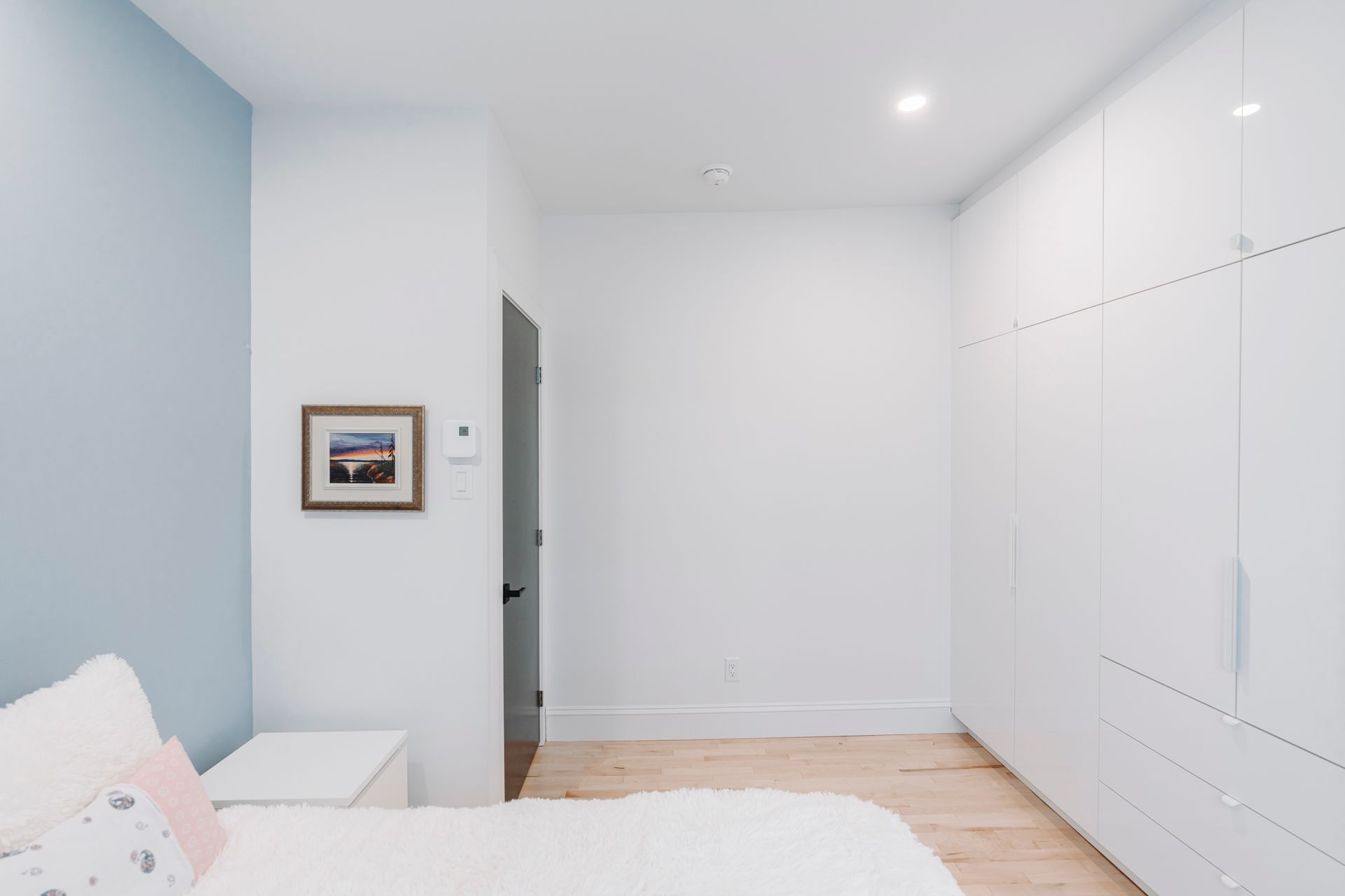 Intérieur de chambre avec mur bleu clair, placard blanc, parquet et lit.
