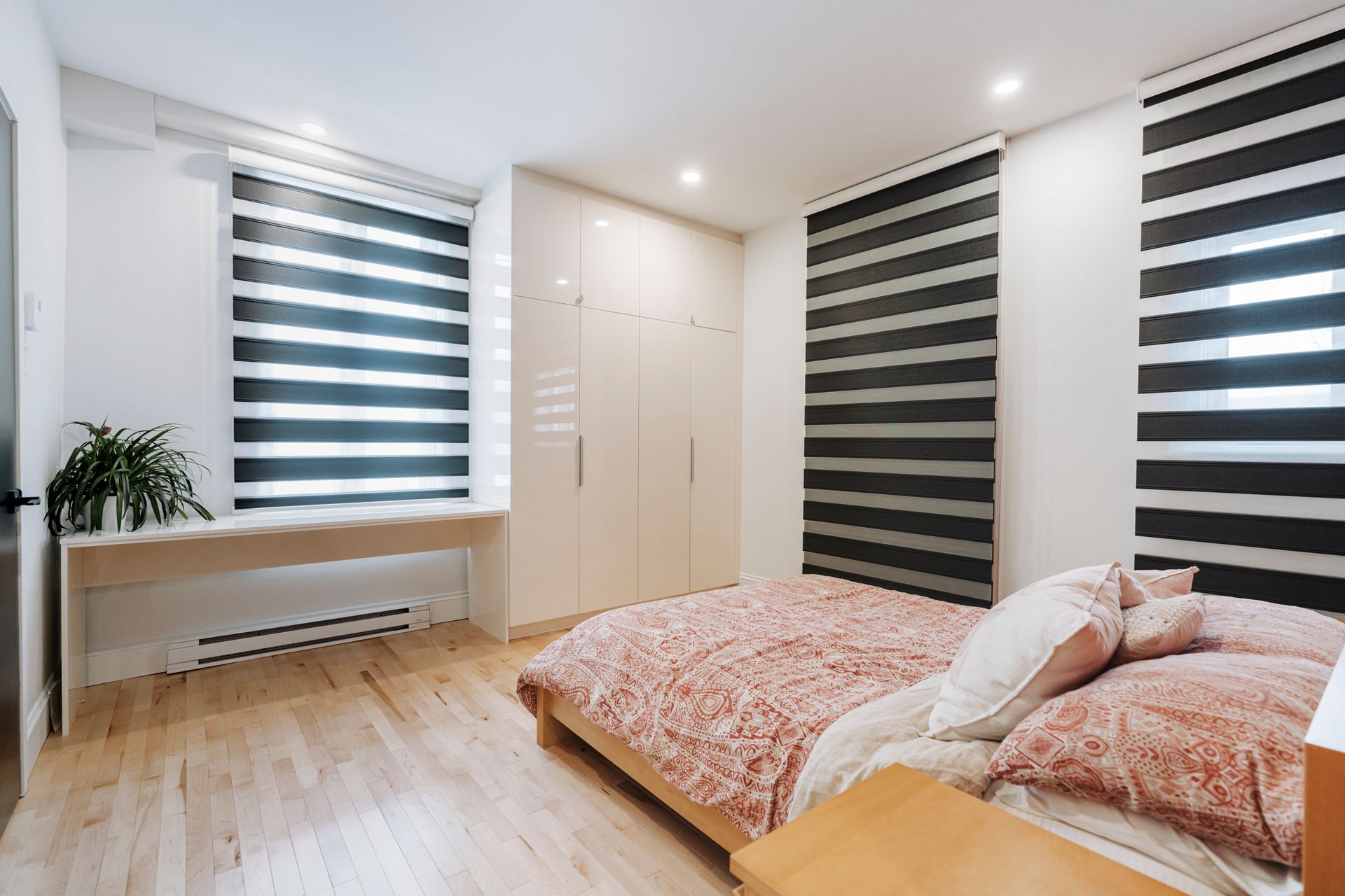 Chambre avec parquet, couvre-lit rose, stores clairs et armoire blanche.