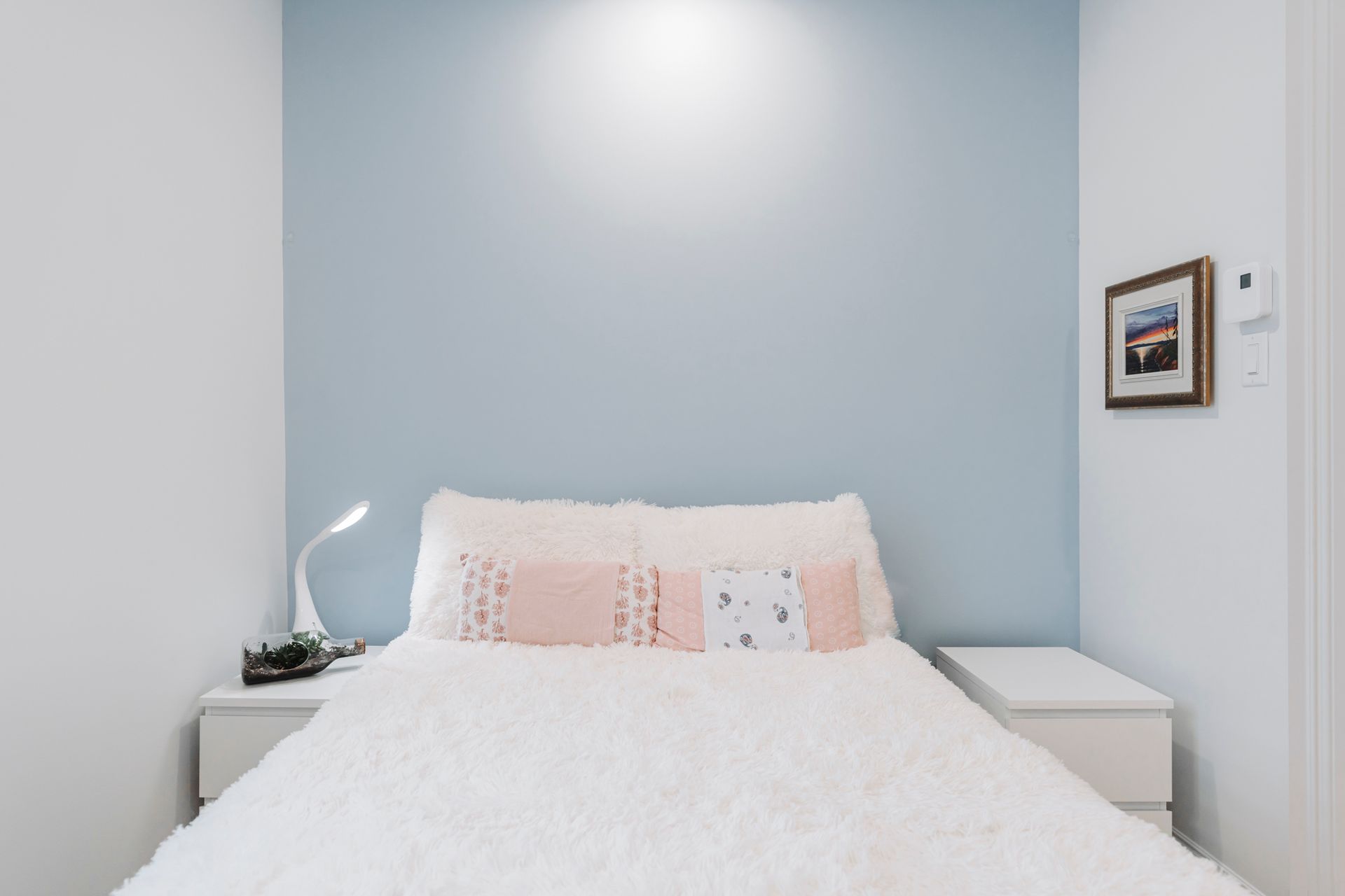 Une chambre bleu clair avec un lit blanc, des tables de nuit et une petite photo encadrée.