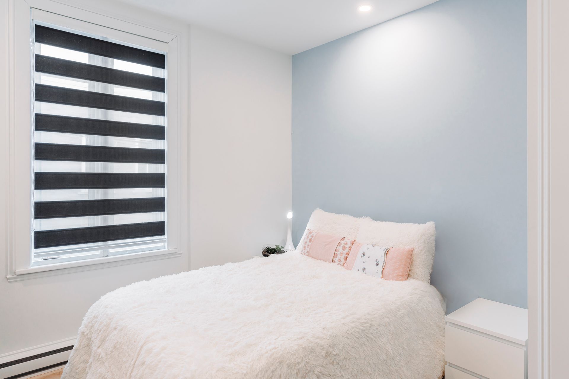 Chambre avec murs blancs, mur d'accent bleu, lit avec couette blanche et store à motifs.