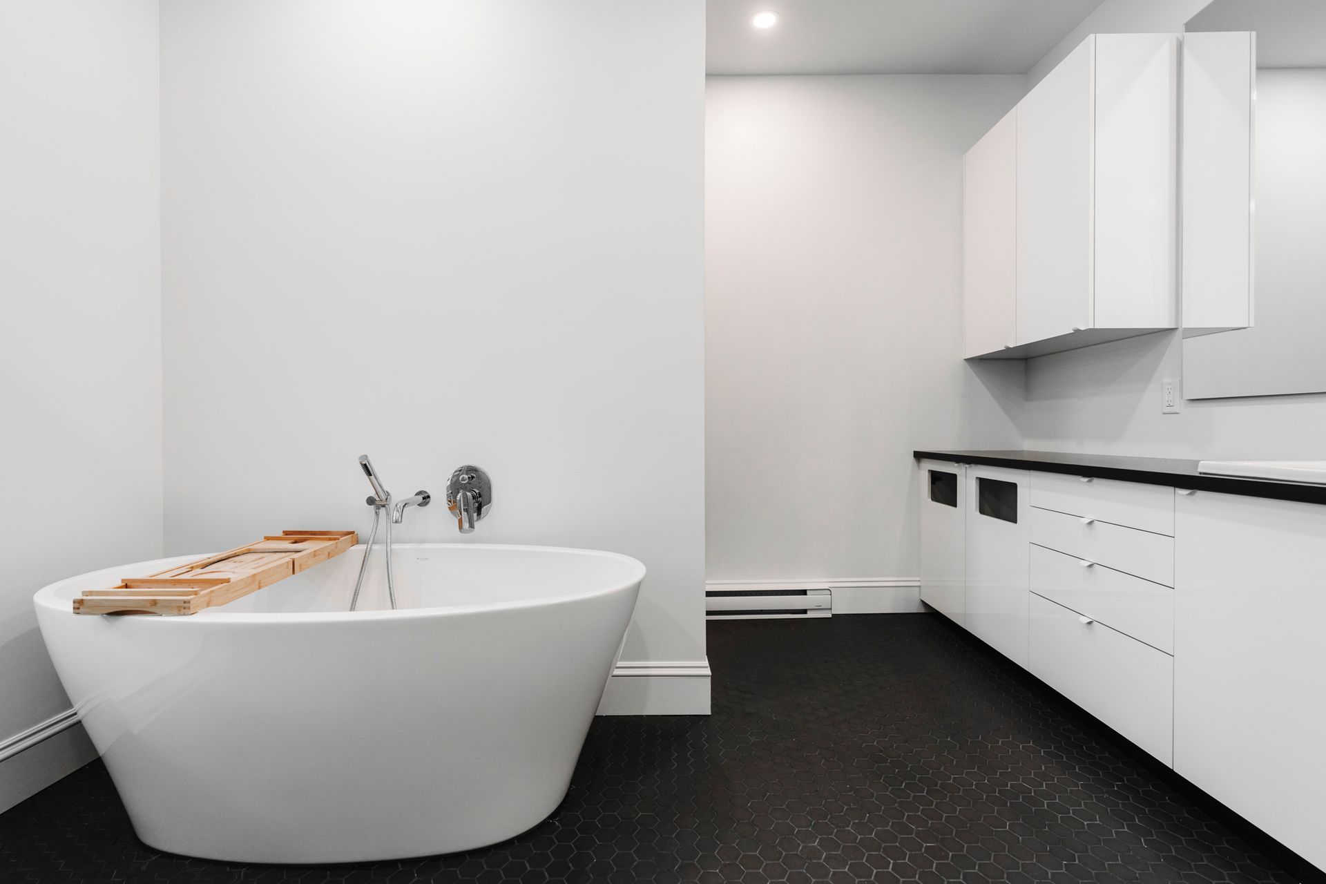Salle de bain moderne blanche avec baignoire et sol noir.