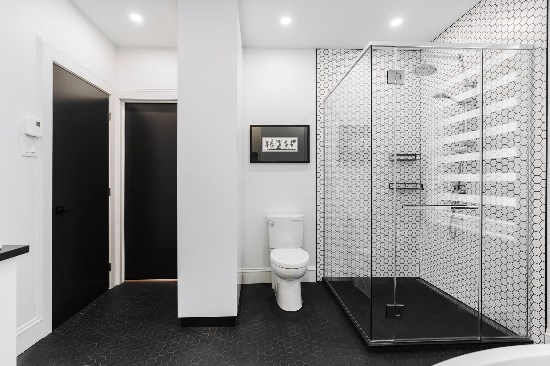 Salle de bain moderne avec sol en carrelage noir, murs blancs, porte noire et douche en verre.