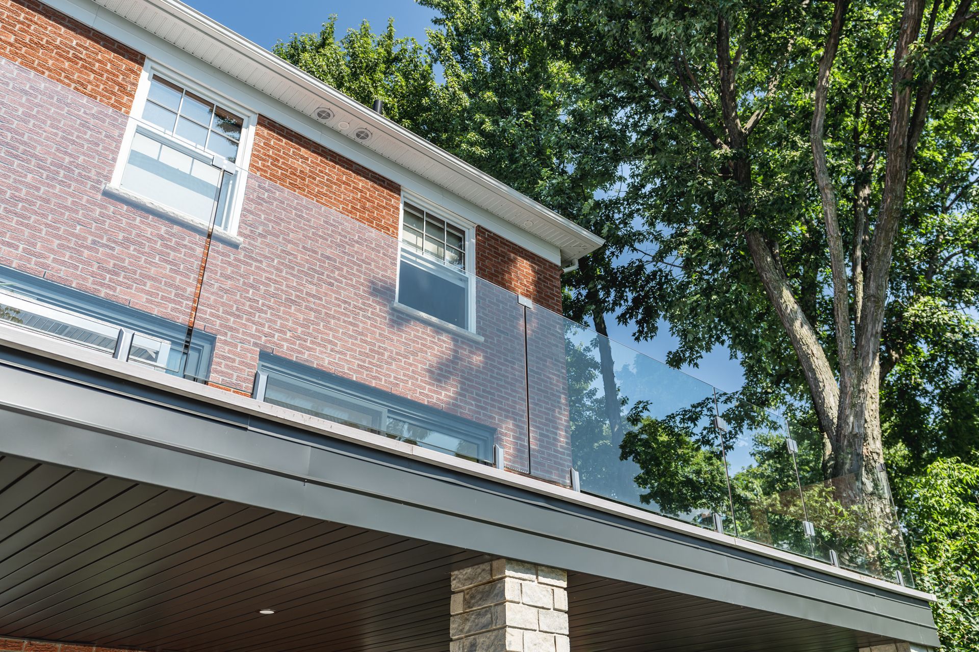 Maison en brique avec balcon vitré, entourée d'arbres.