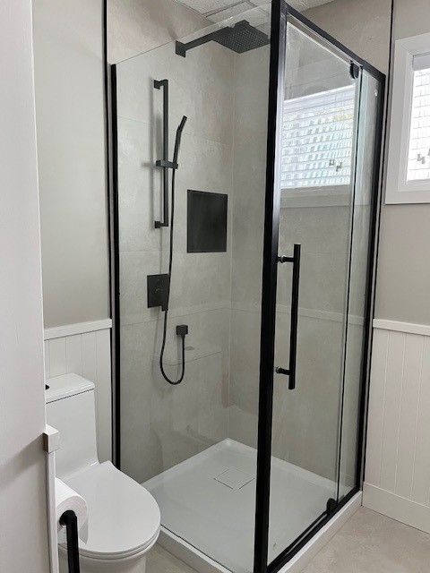 Salle de bain moderne avec douche à cadre noir, toilettes et rangement de douche intégré.