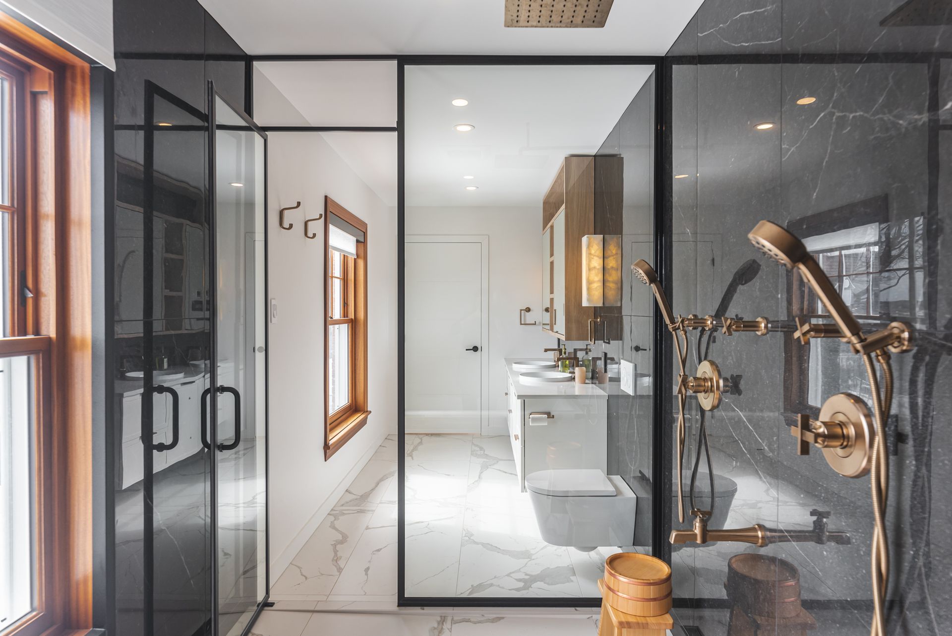 Salle de bain moderne et luxueuse avec douche à cadre noir, marbre et accessoires dorés.