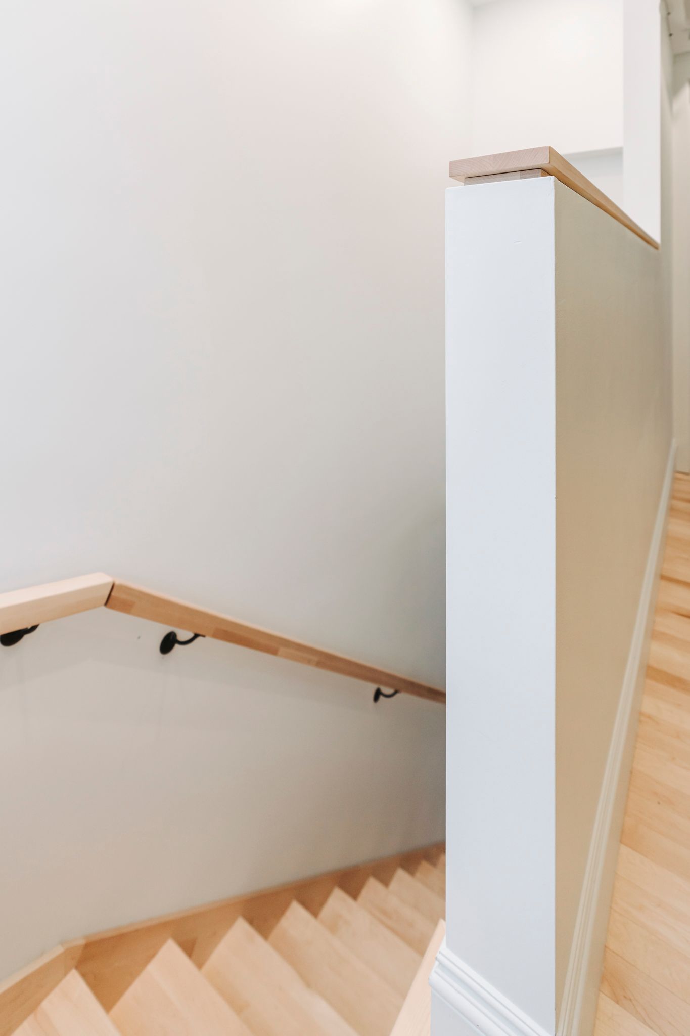 Escalier avec marches en bois clair, murs blancs et rampe en bois.