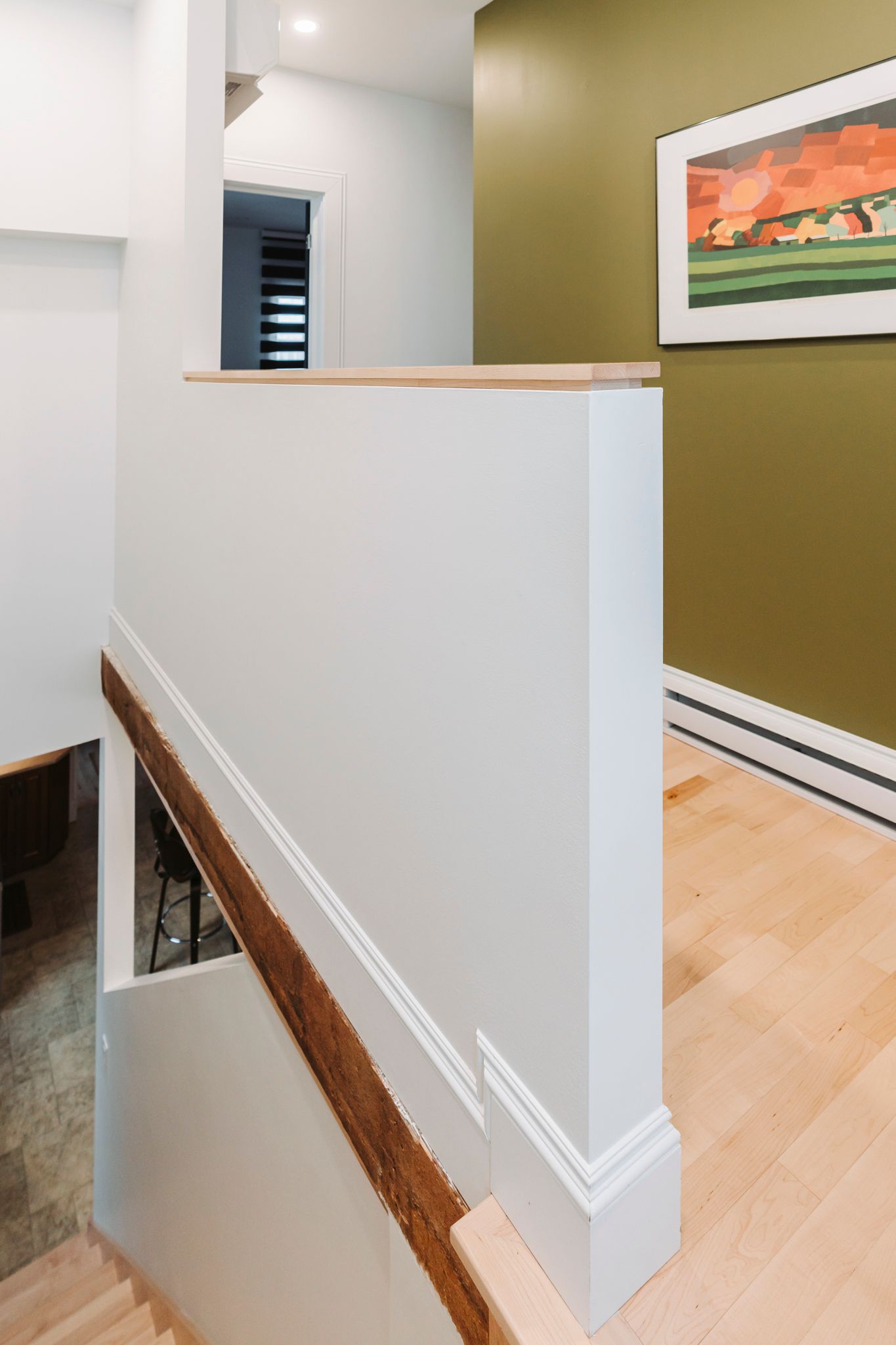 Escalier avec mur blanc et rampe en bois. Mur végétalisé avec œuvre d'art en arrière-plan.
