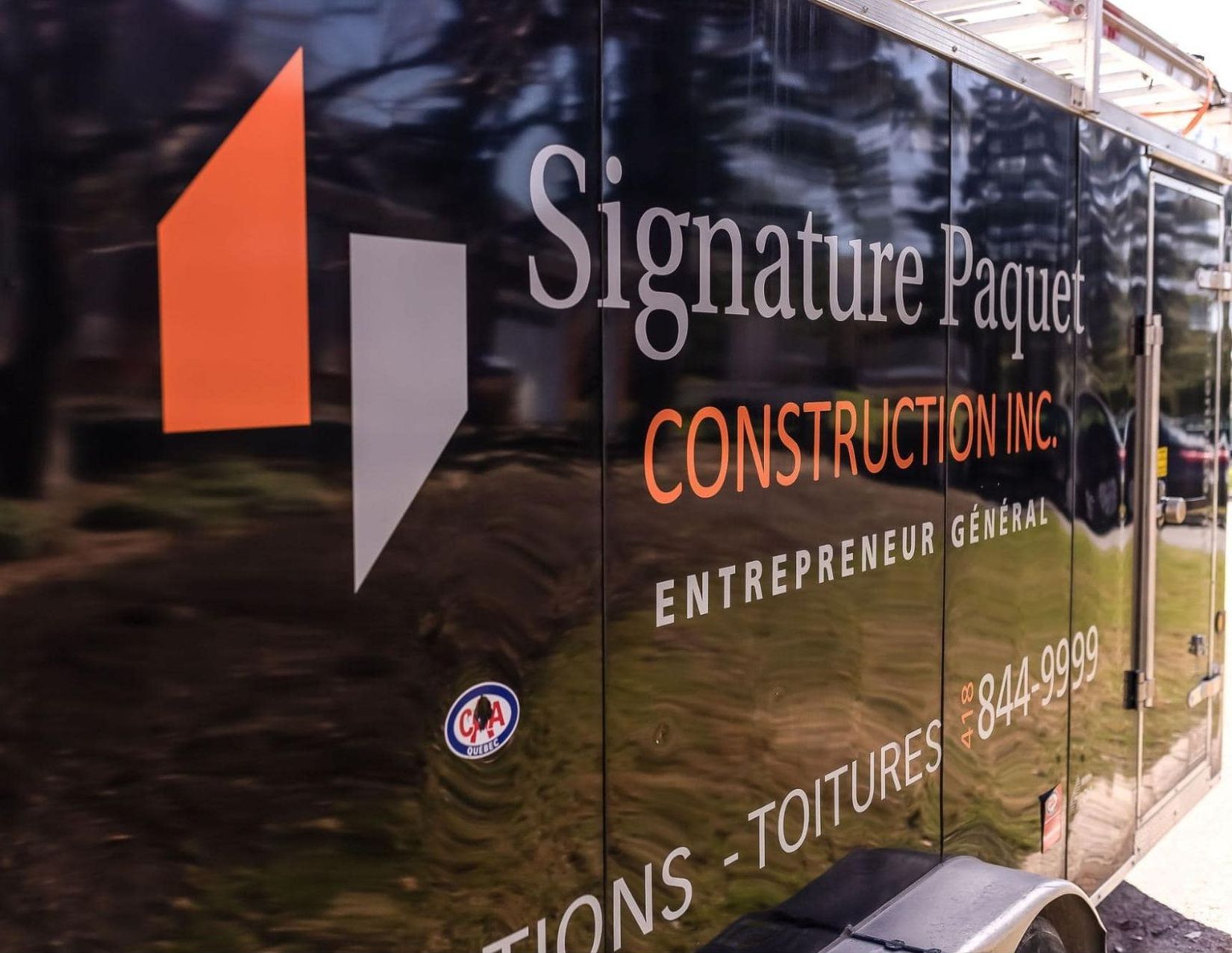 Une remorque pour signature paquet construction inc. est garé sur le bord de la route.