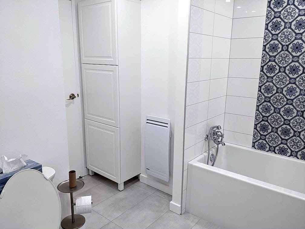 Petite salle de bain blanche avec un grand meuble de rangement, une baignoire et des toilettes. Rideau de douche bleu et blanc.