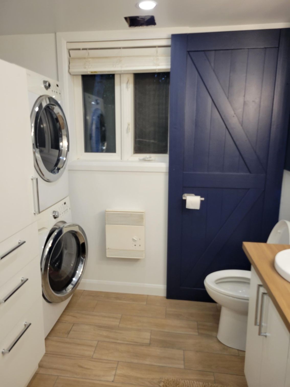 Buanderie avec laveuse/sécheuse superposées, porte de grange bleue et toilettes.
