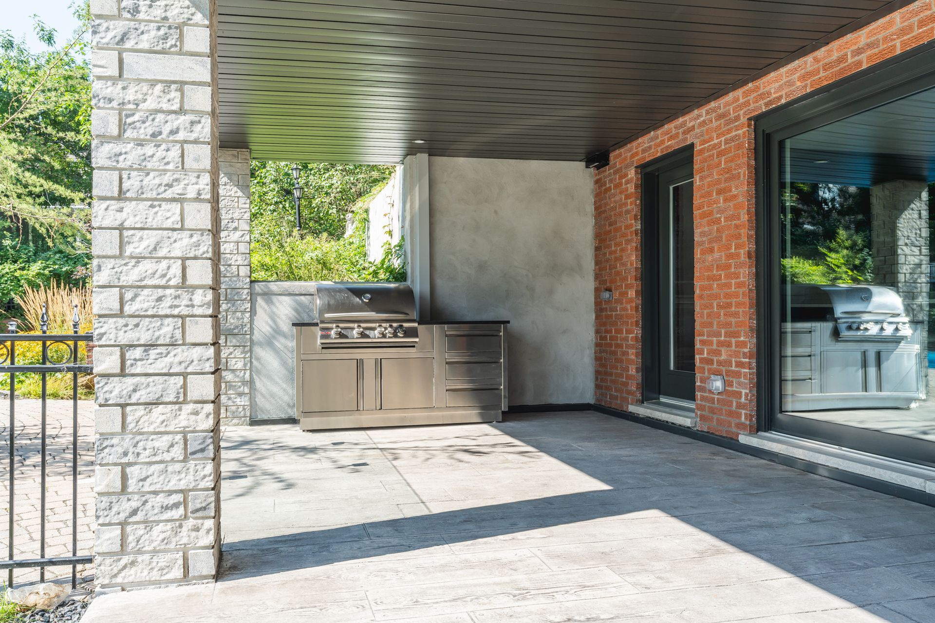 Terrasse extérieure avec barbecue intégré, piliers en pierre et mur de briques rouges.