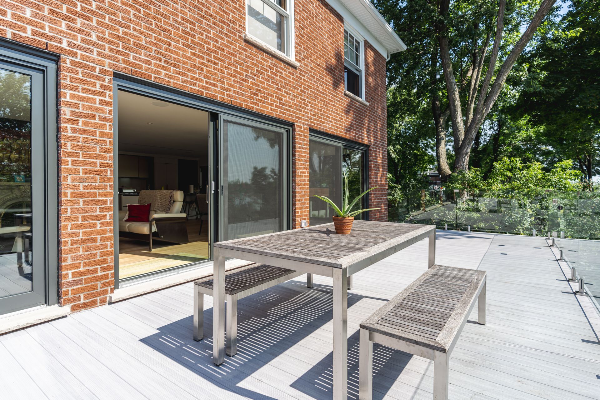 Maison en briques rouges avec une terrasse et des portes coulissantes en verre ouvrant sur une table à manger et des bancs.