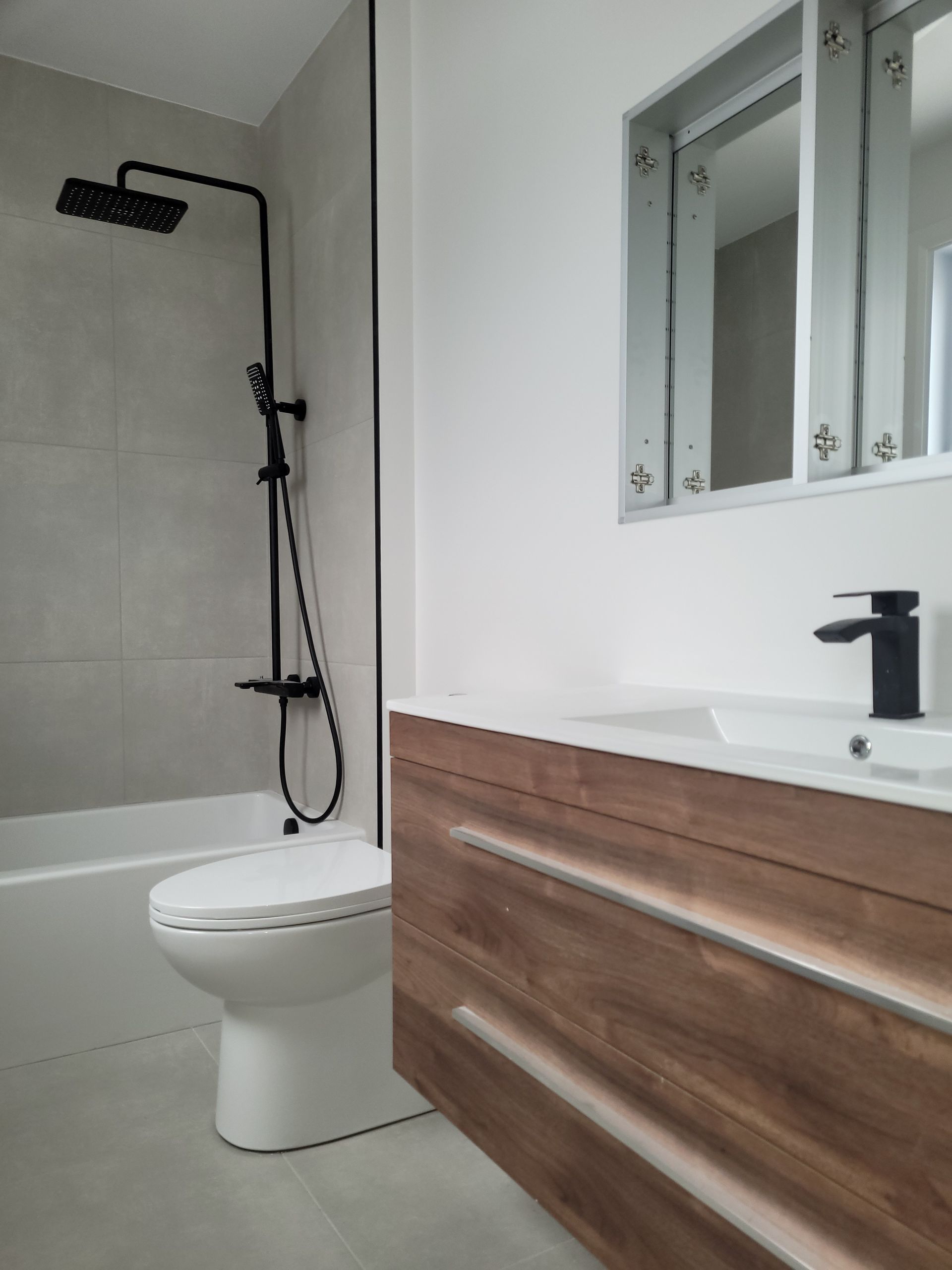 Salle de bain moderne avec luminaires noirs, vanité en bois et douche carrelée grise.