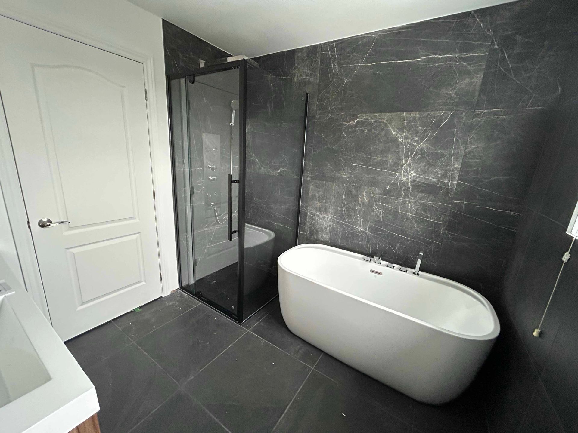 Salle de bains moderne avec murs carrelés noirs, douche en verre et baignoire blanche.