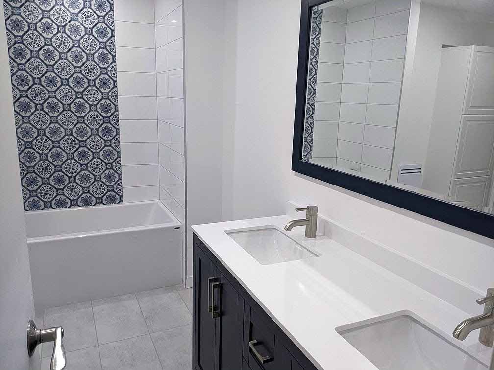 Salle de bain avec carrelage à motifs bleus et blancs, meuble-lavabo double et grand miroir.