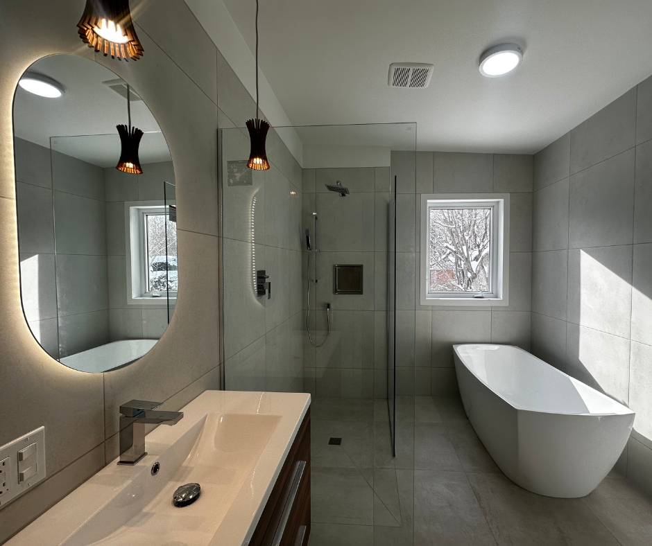 Salle de bain moderne avec baignoire autoportante, douche en verre et grand miroir ovale avec éclairage chaleureux.