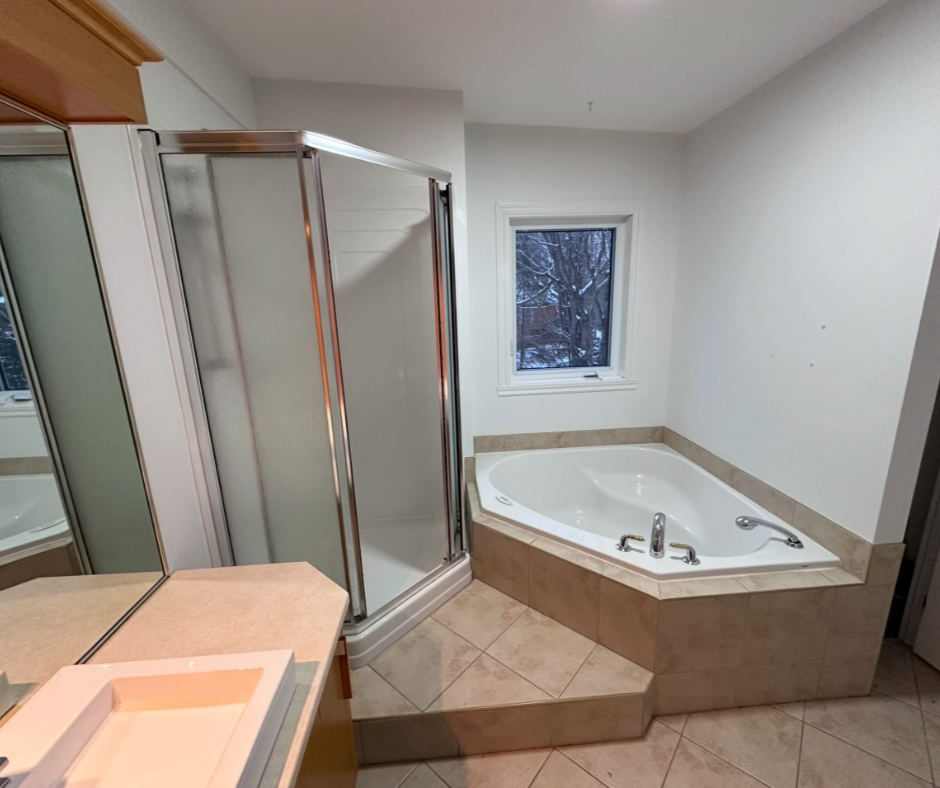 Salle de bain avec douche en verre, baignoire jacuzzi d'angle et fenêtre.