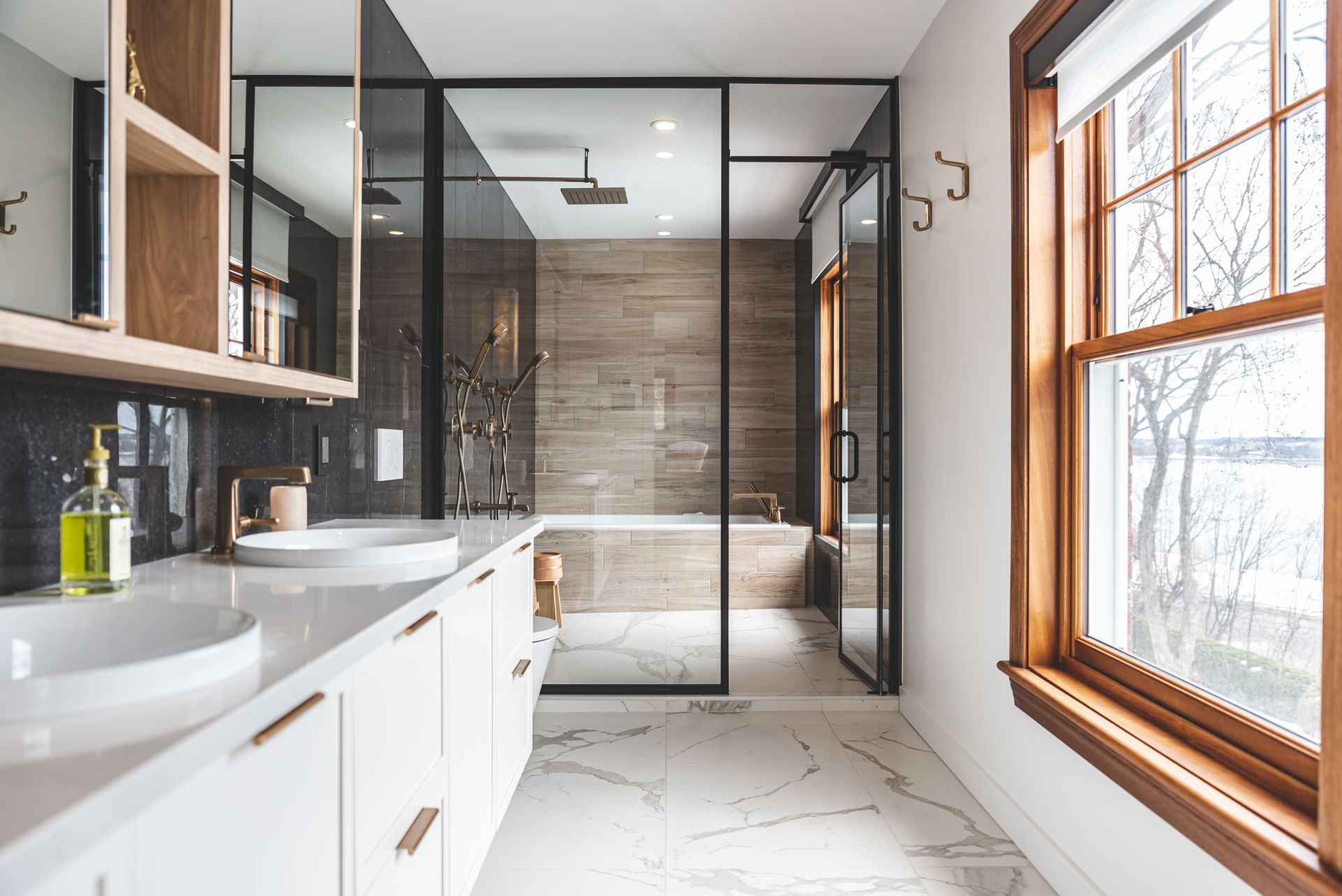 Salle de bain moderne avec douche en verre, armoires blanches, sol en marbre et vue sur la fenêtre.