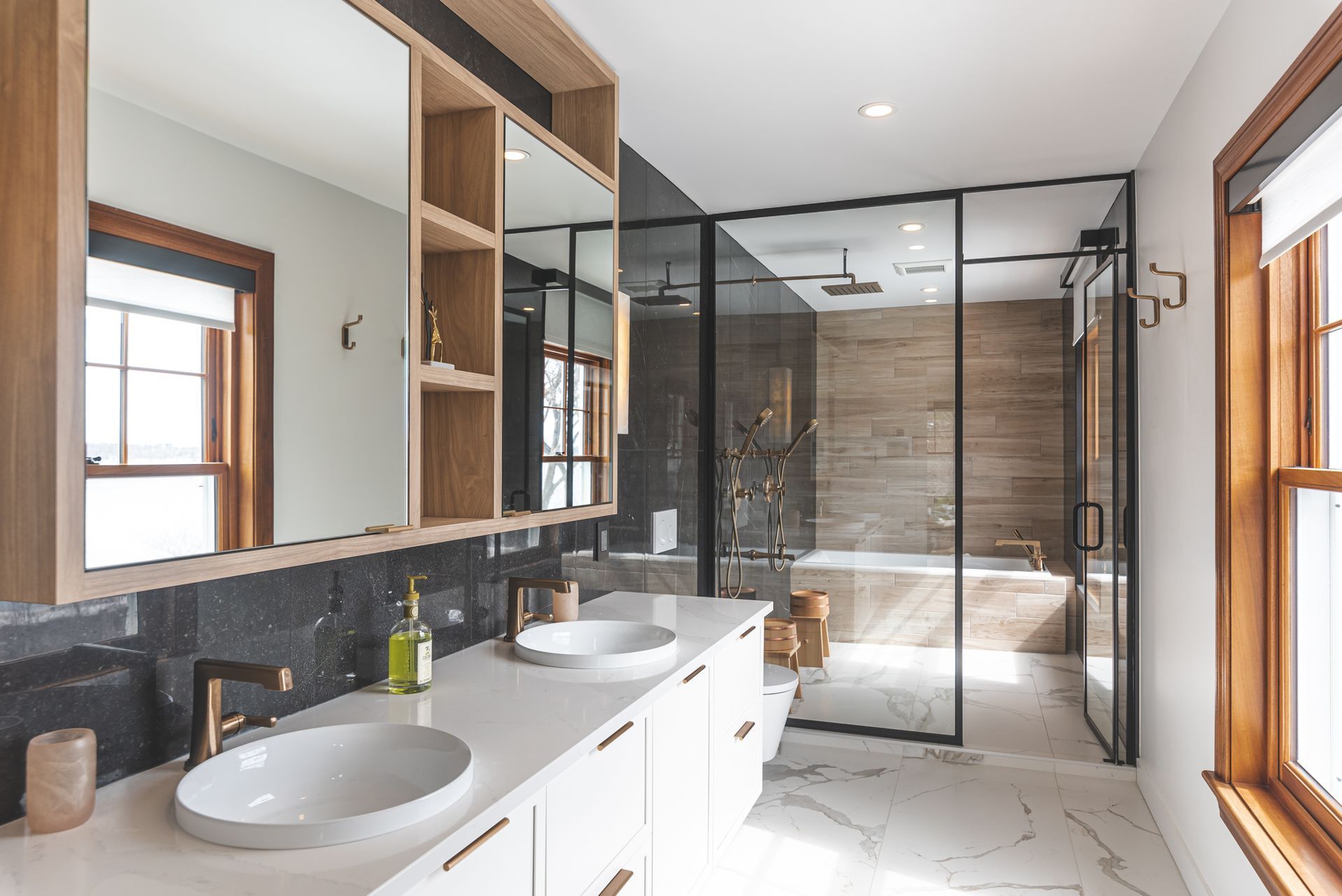 Salle de bain moderne avec vanité blanche, accents de bois, douche en verre et grands miroirs.