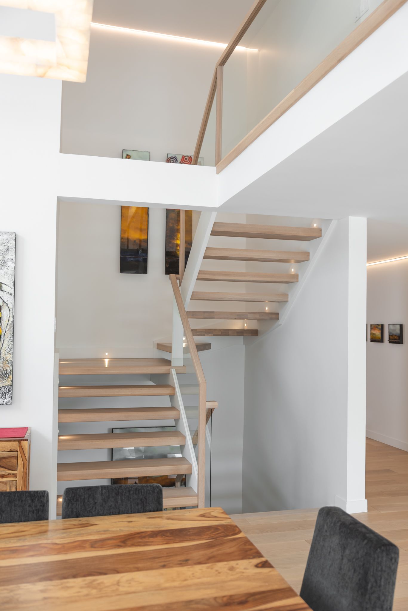 Intérieur moderne avec escalier en bois menant à une mezzanine, murs blancs et table à manger.